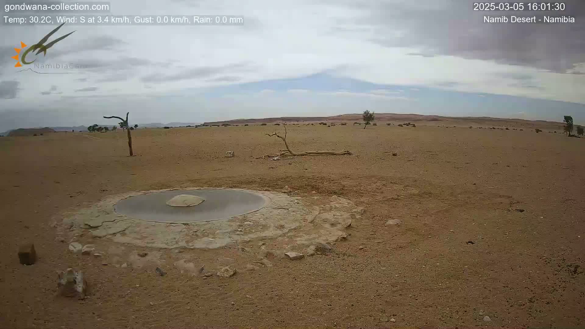 A circular, flat structure sits in a sandy desert under a mostly cloudy sky.