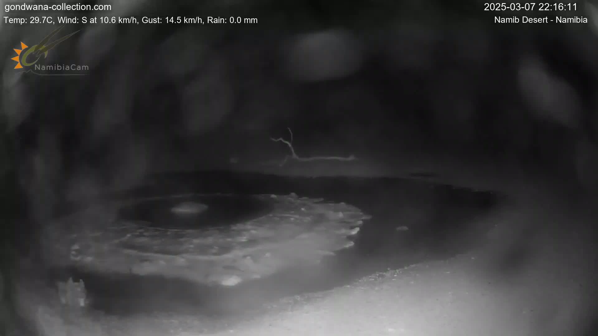 A nighttime, low-light image shows a dark, sandy or rocky area with a patch of lighter-colored, possibly wet, ground in the center, under a clear sky with a south wind.