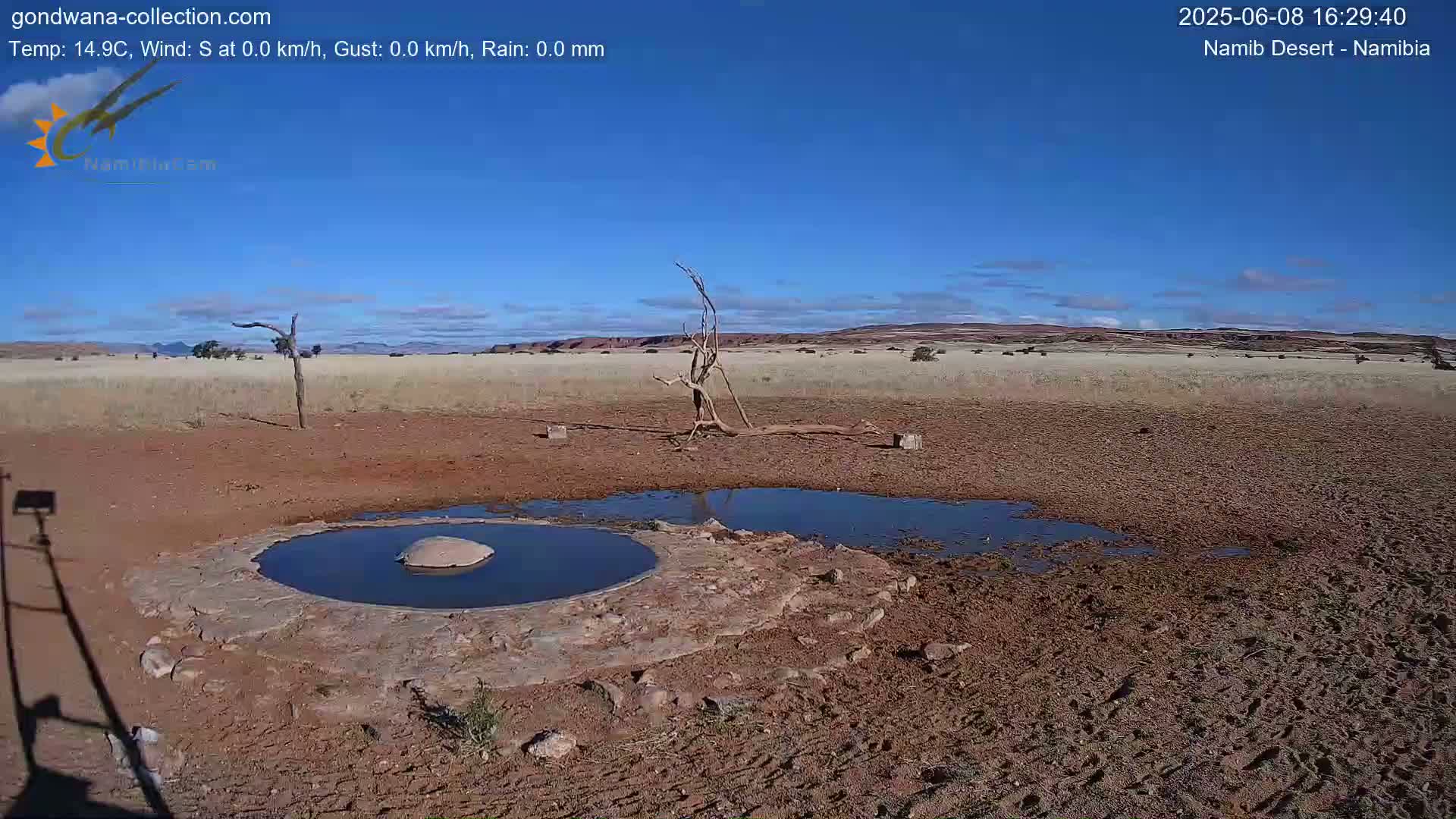 A small, shallow pool of water sits in the center of a dry, dusty landscape under a clear blue sky.