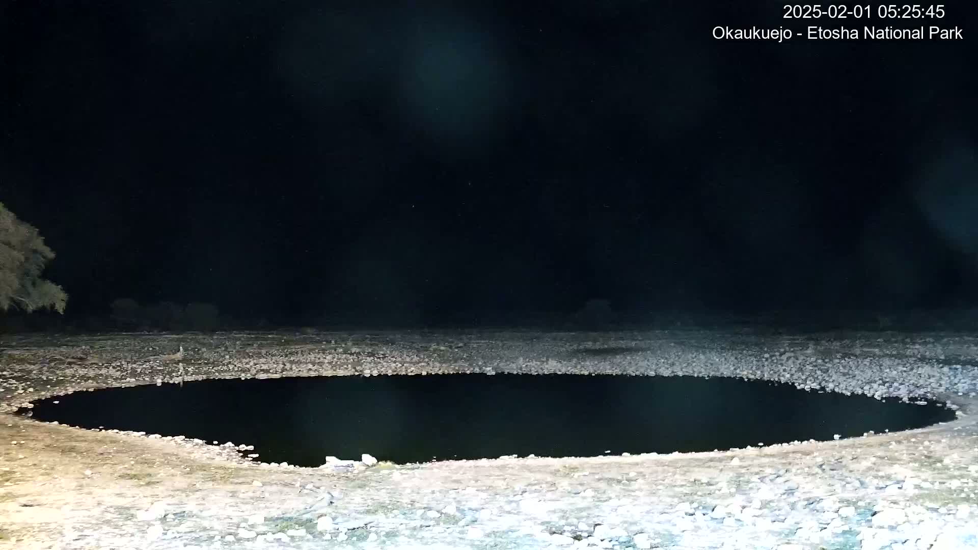 A dark, circular pool of water sits in a rocky, flat landscape under a clear, night sky.