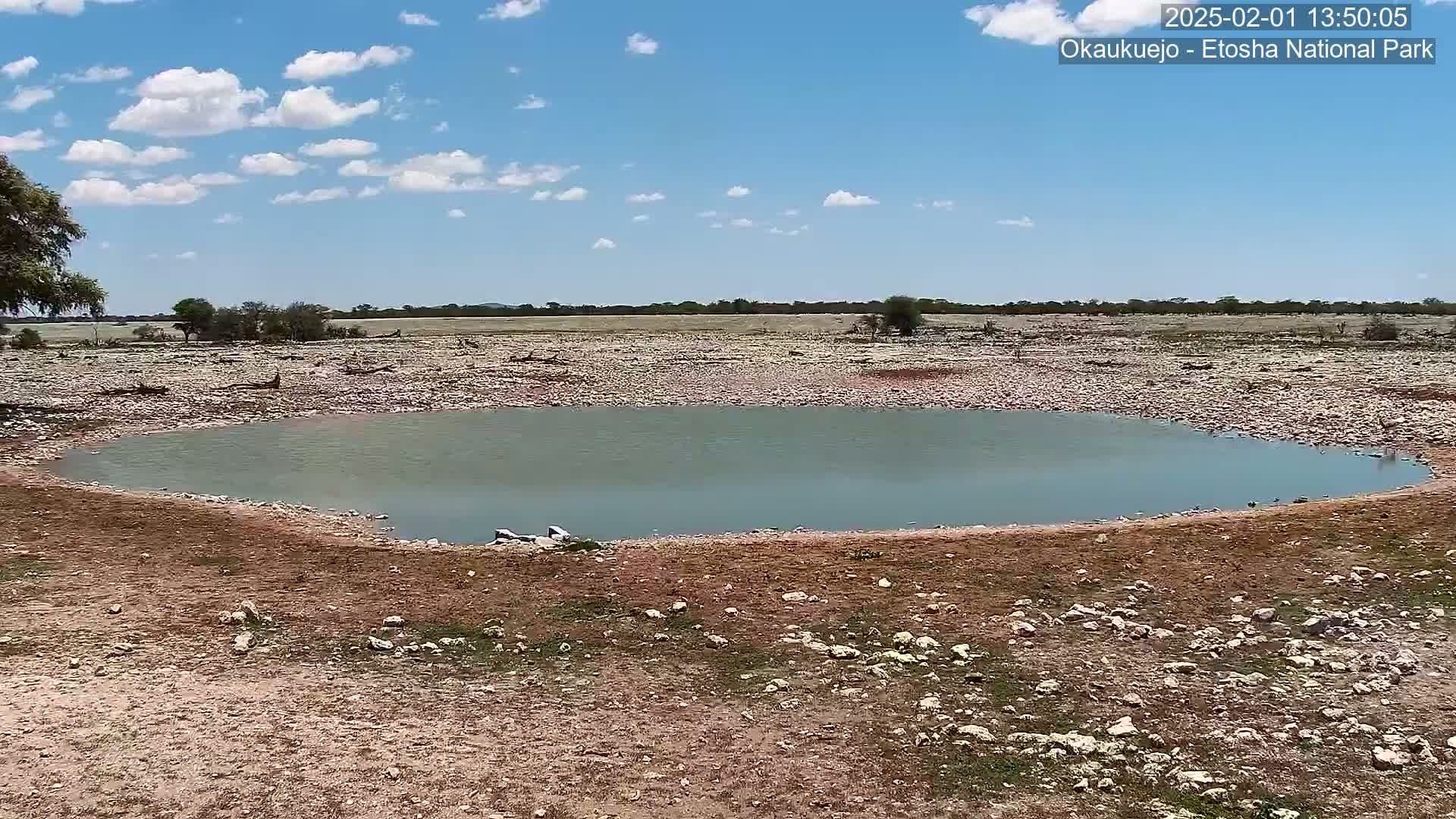 A small, calm body of water sits in a rocky, dry landscape under a partly cloudy sky.