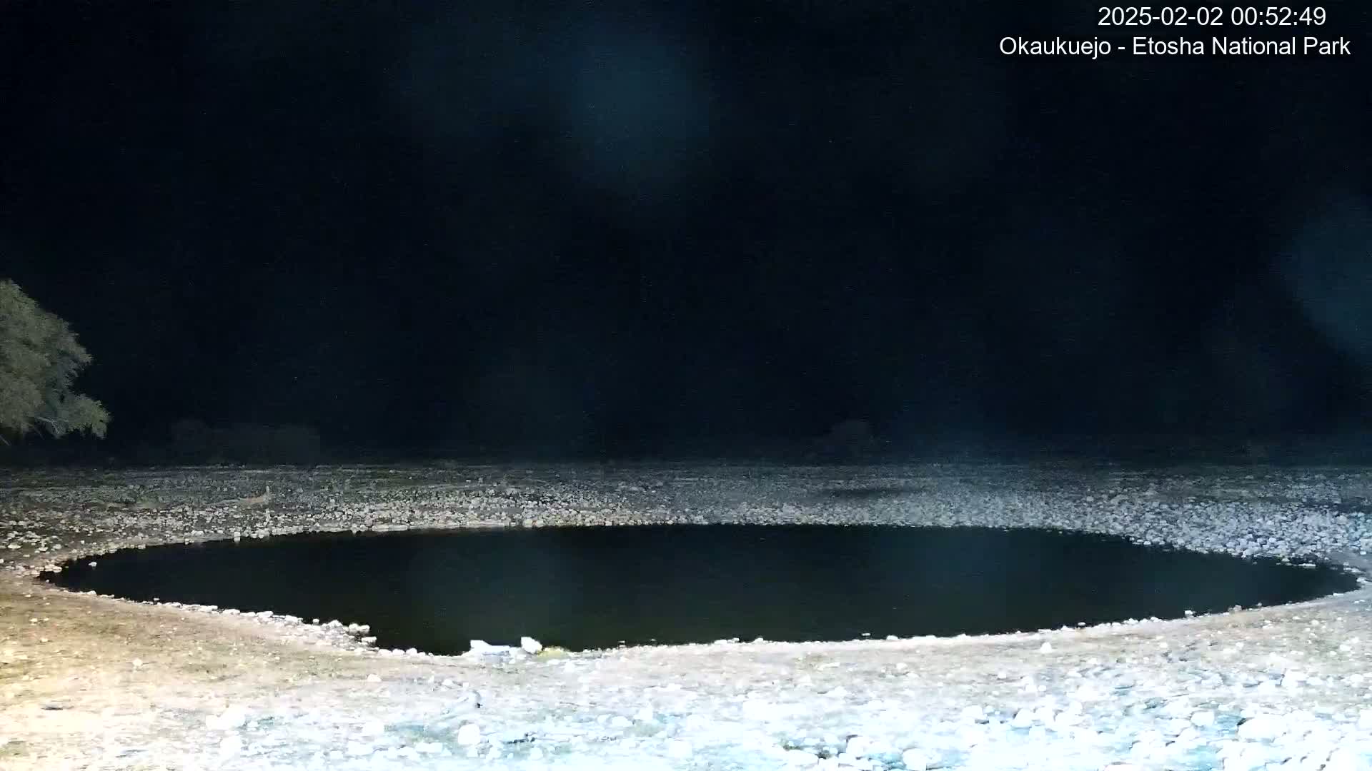 A dark, circular pool of water sits in a rocky, dry landscape at night.