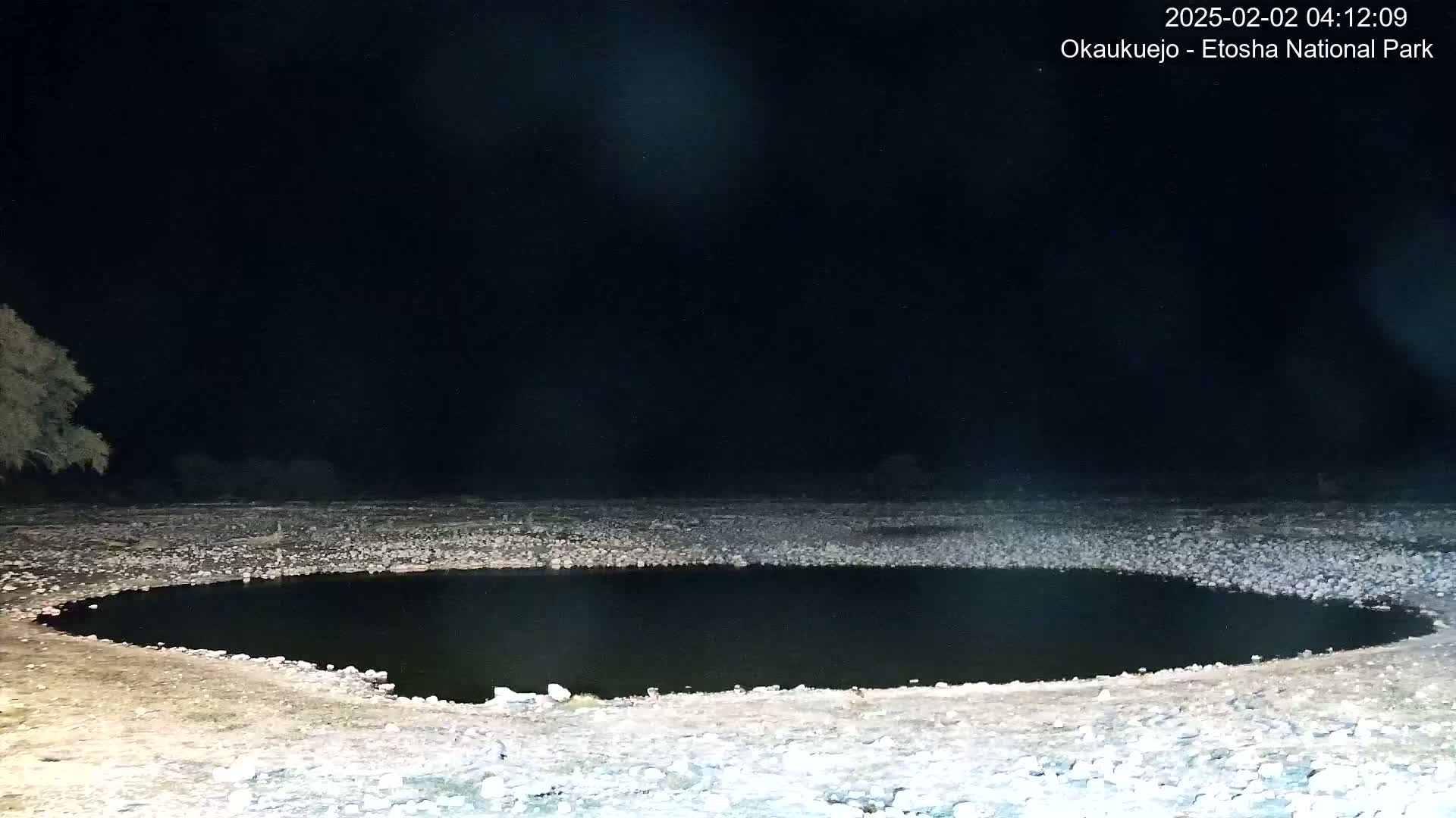 A dark, circular pool of water sits in a rocky, flat landscape at night.
