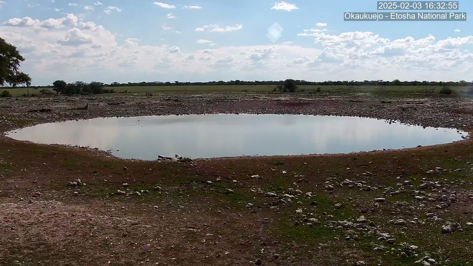 A small, calm pool of water sits in a rocky, dry landscape under a partly cloudy sky.