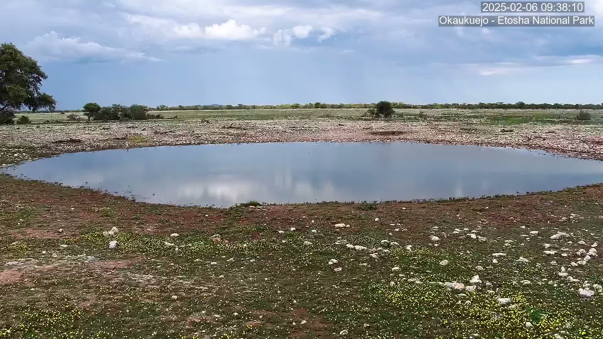 A calm, shallow pool of water reflects a cloudy sky in a rocky, sparsely vegetated landscape.