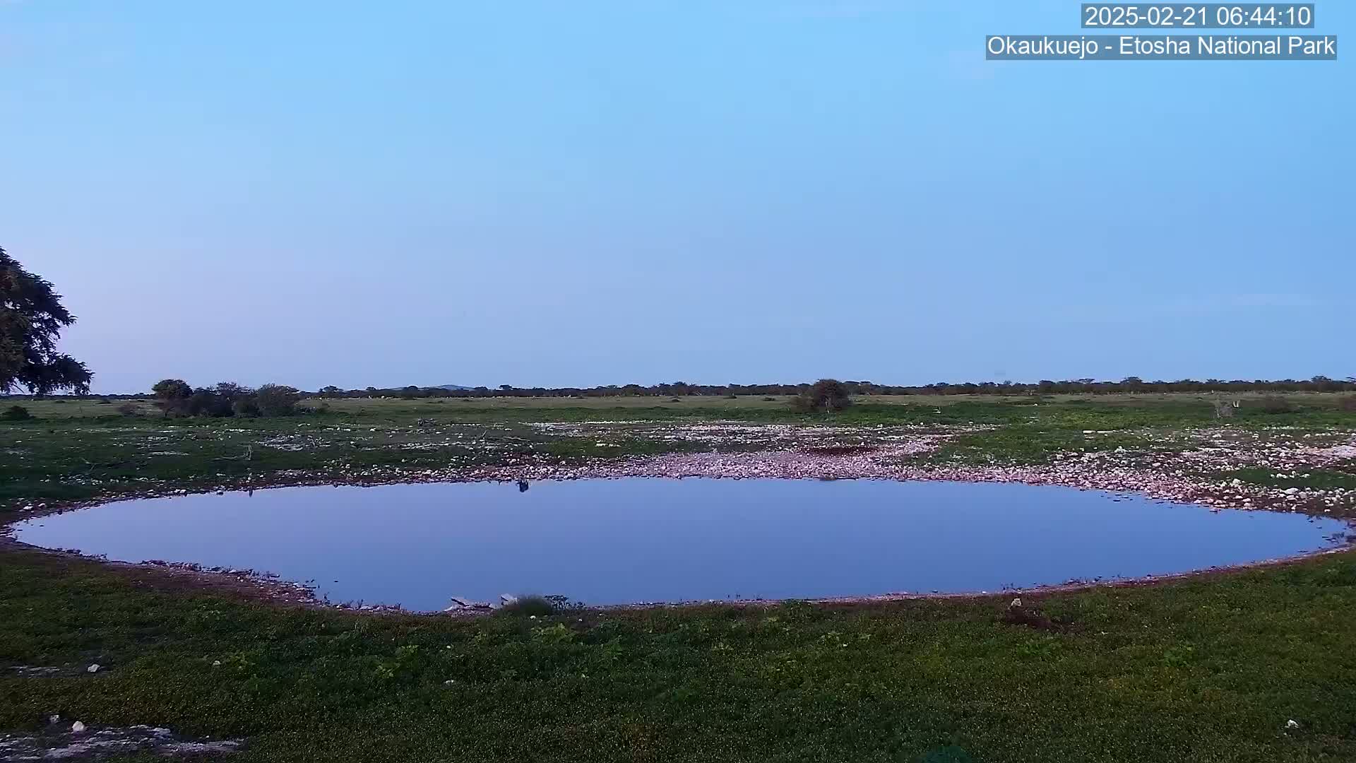 A calm, blue-reflective pool of water sits in a grassy, rocky expanse under a clear twilight sky.