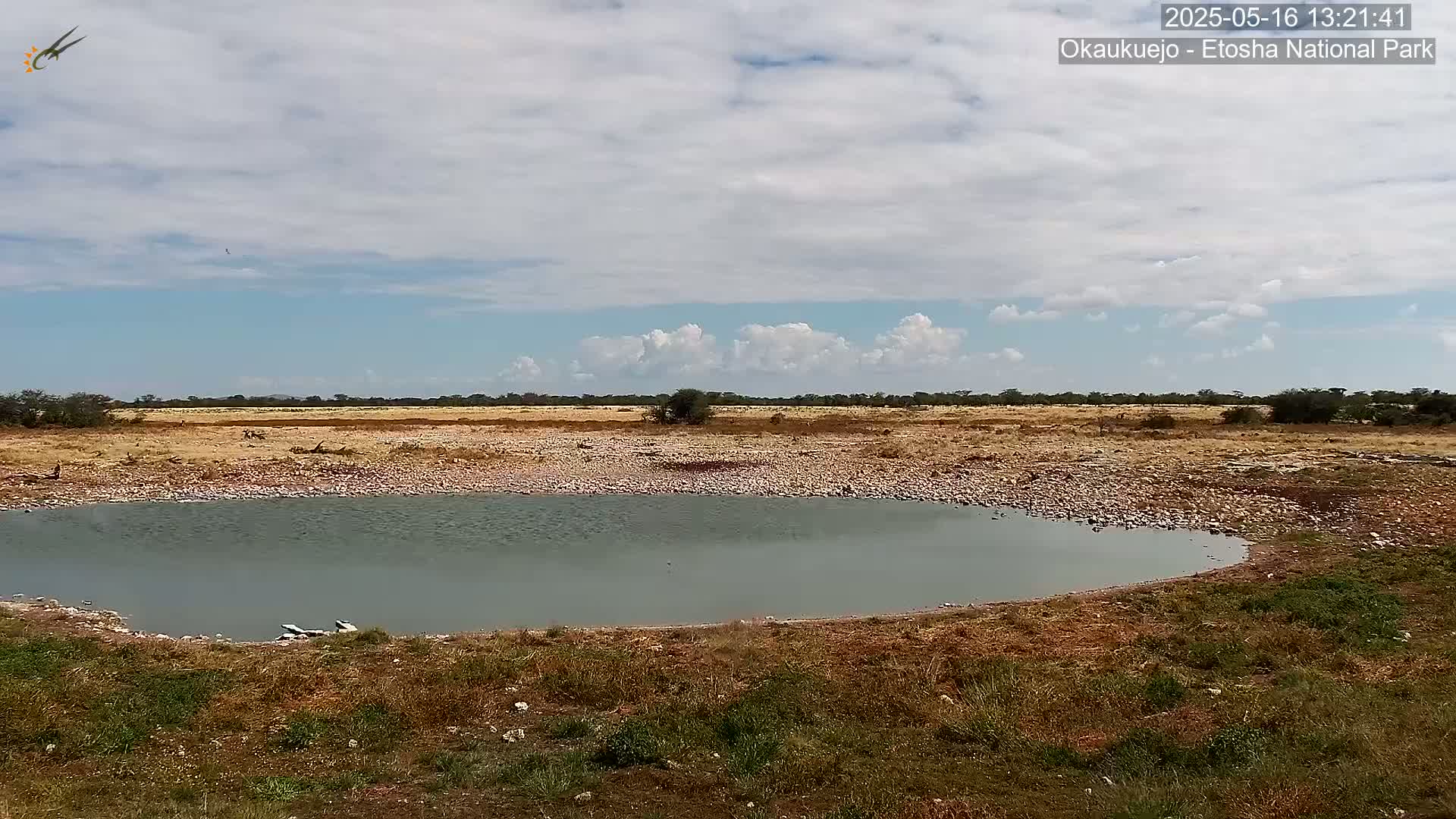 A small, still body of water sits in a dry, rocky landscape under a partly cloudy sky.