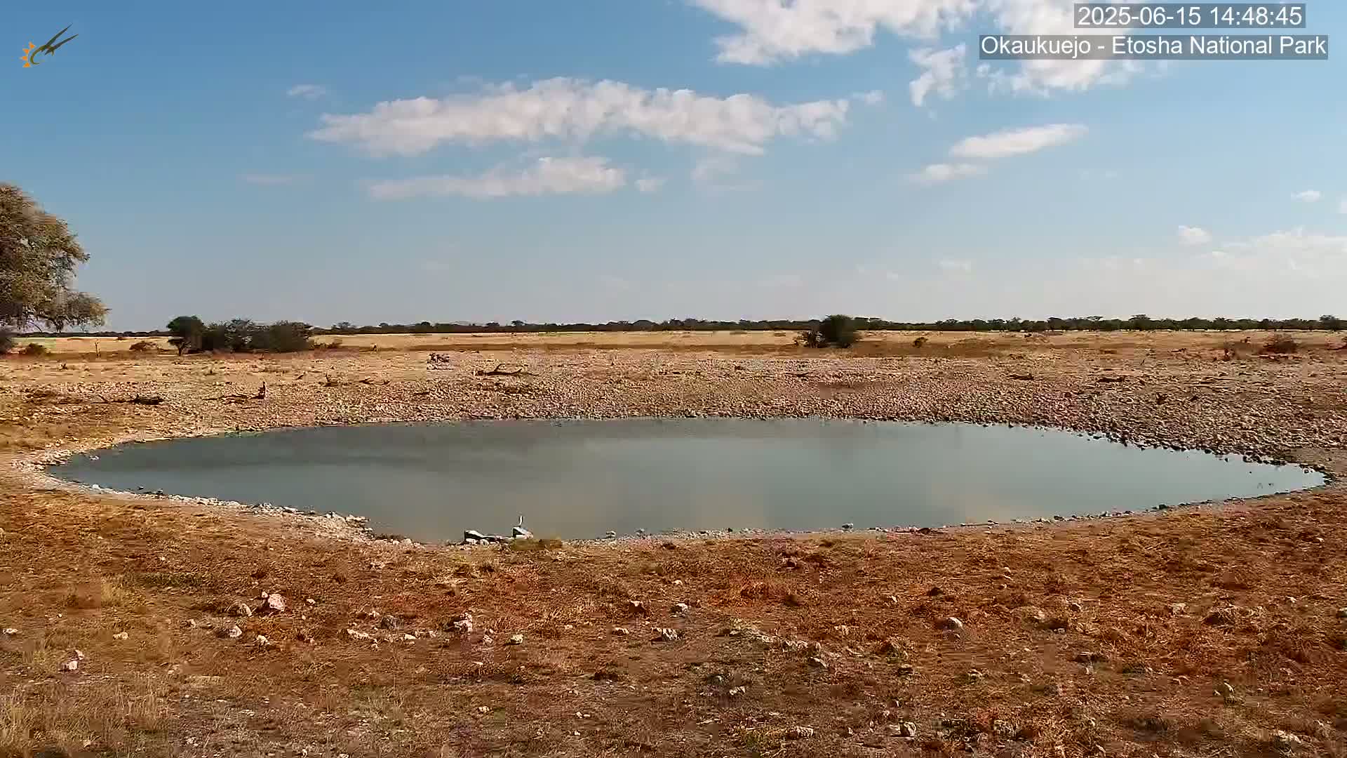 A small, calm body of water sits in a dry, rocky landscape under a partly cloudy sky.