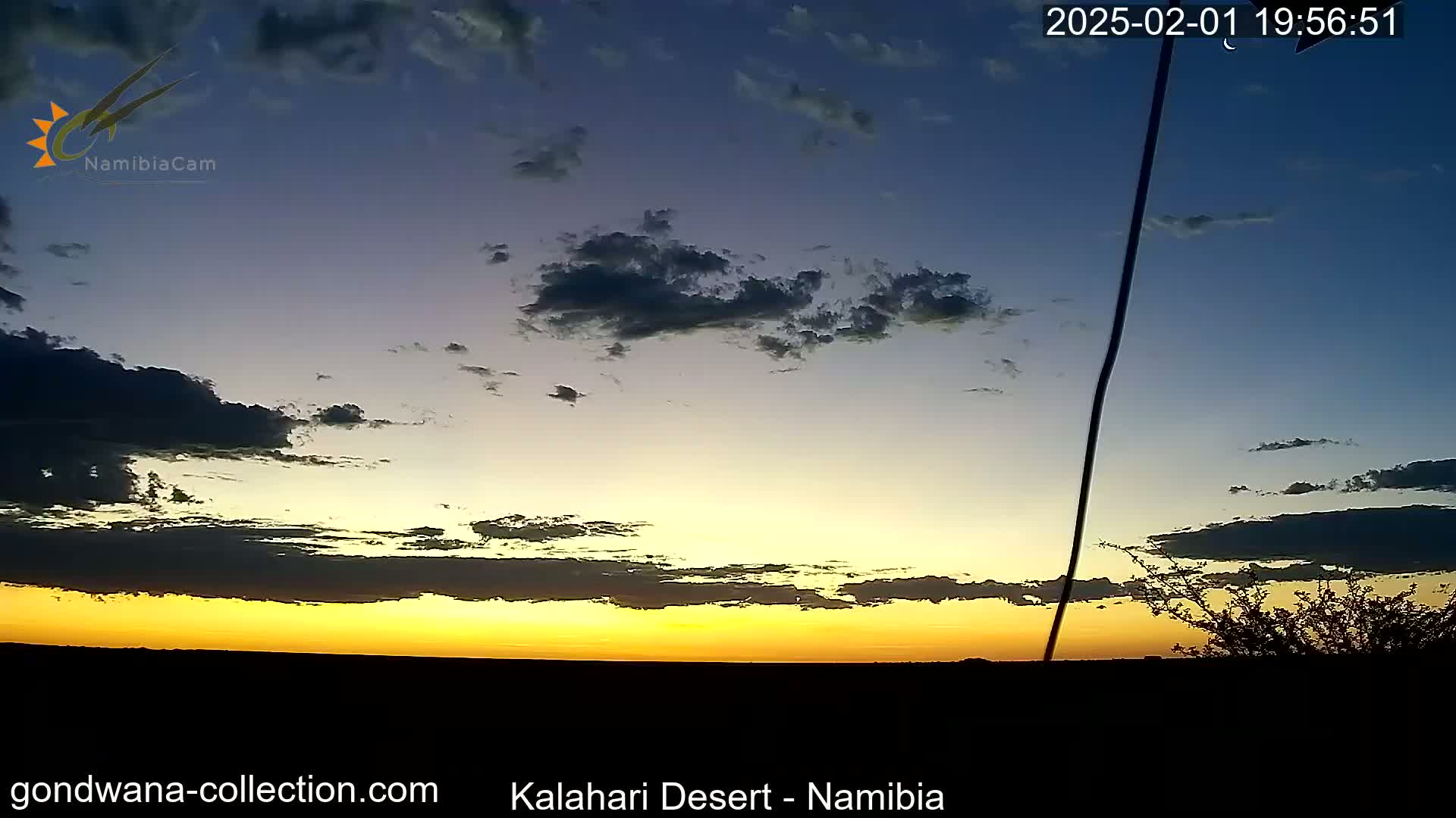 A vibrant sunset casts a golden glow across a mostly clear desert sky, with a few dark clouds lingering above the horizon.