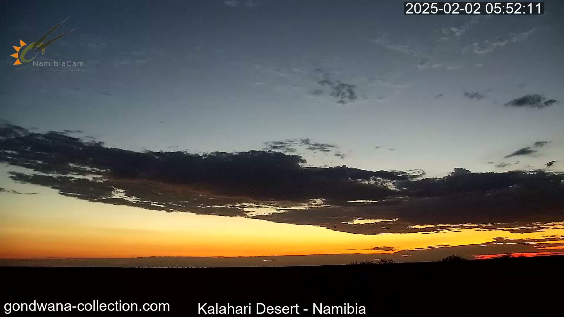 A partly cloudy sunset with orange and yellow hues over a dark, flat landscape.