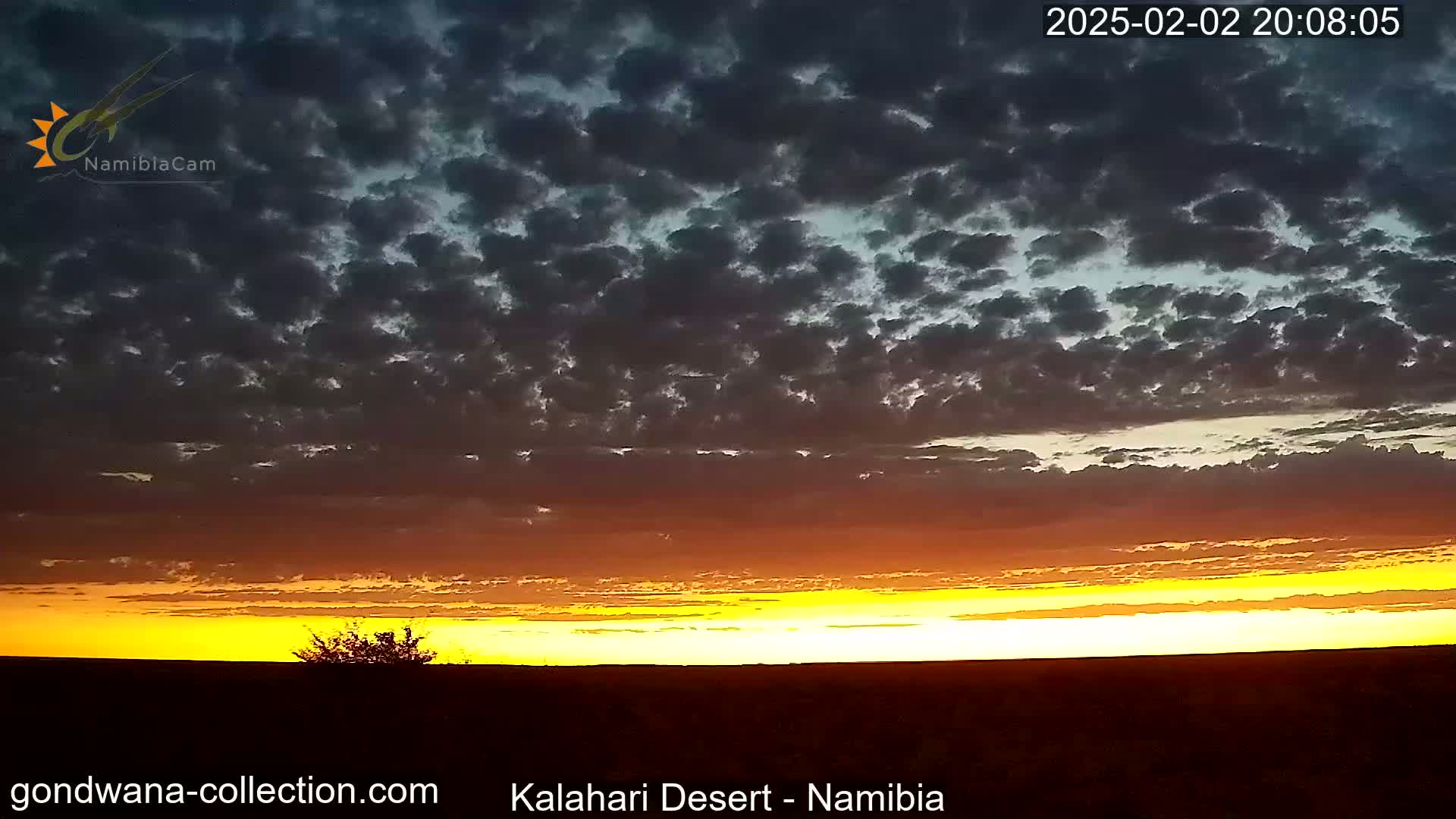 A fiery sunset with a mostly cloudy sky casts an orange and yellow glow over a flat, dark landscape.