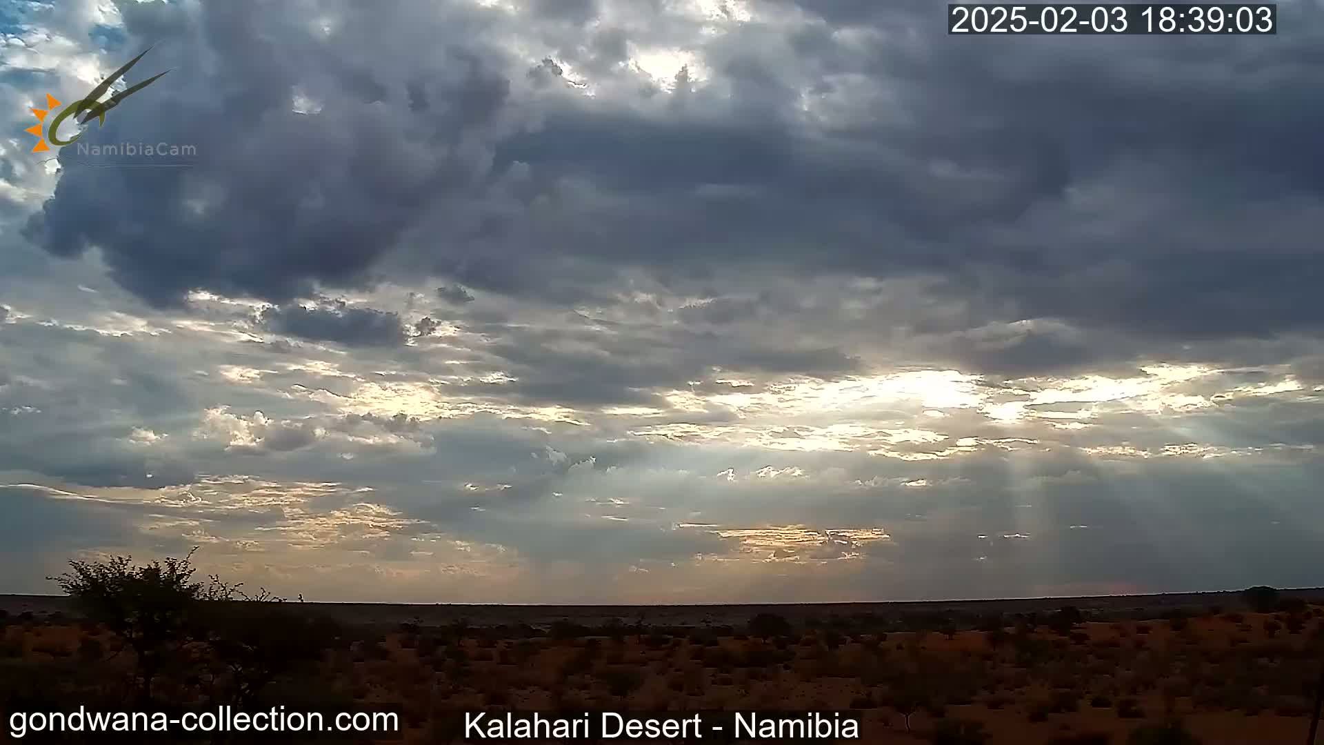 Sunbeams break through a partly cloudy sky over a flat, arid landscape.