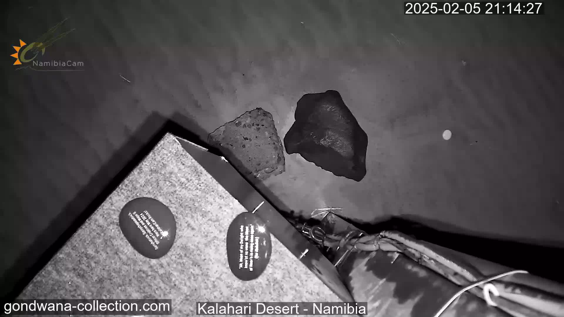 A nighttime, low-angle, black and white view shows two dark rocks on the ground near a stone structure with a circular plaque.