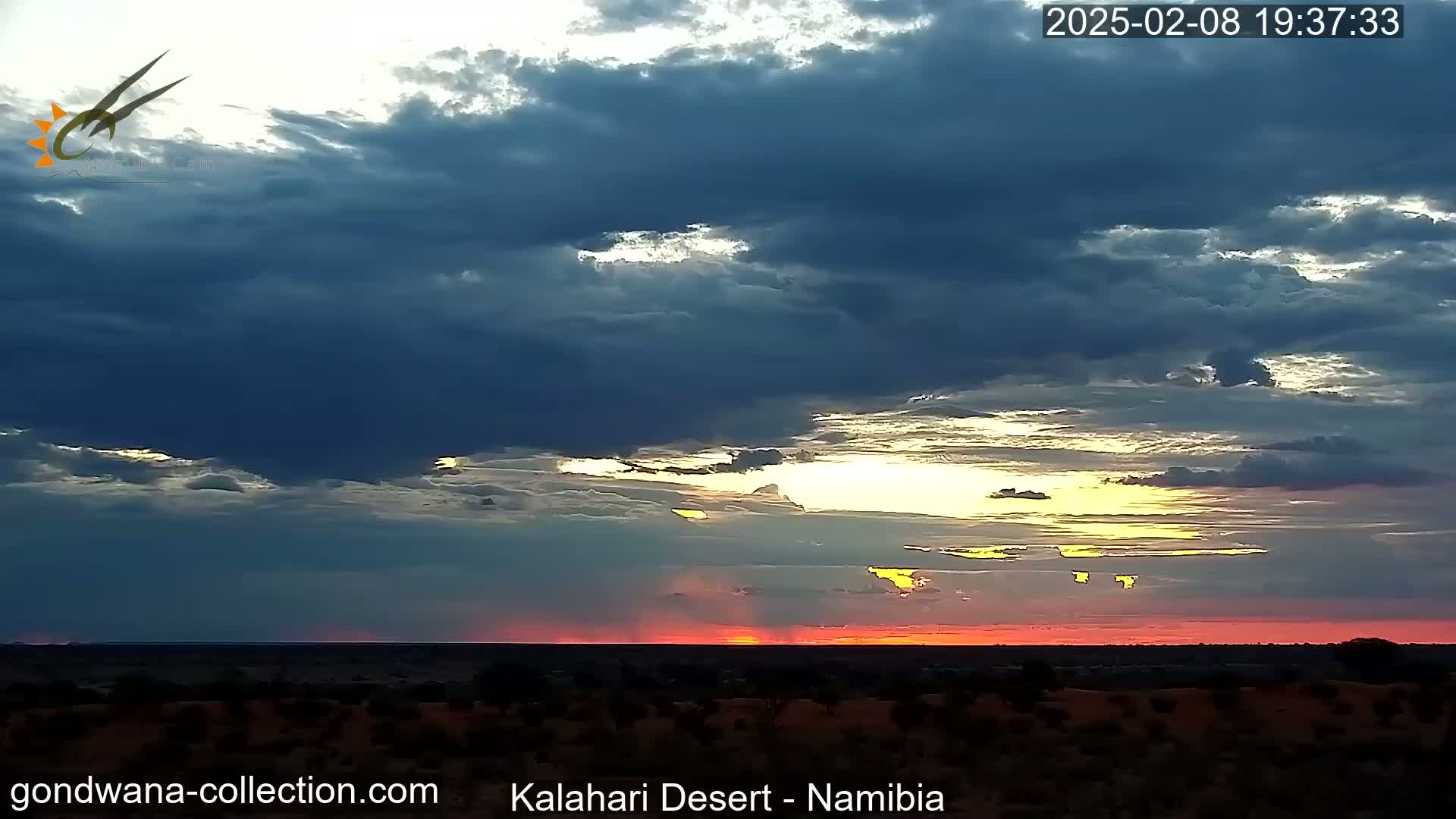 A vibrant sunset with streaks of red and orange illuminates the cloudy sky over a flat desert landscape.