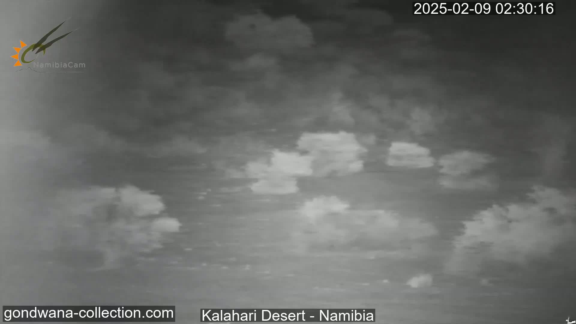 A grayscale image shows a cloudy, nighttime sky over a flat, desert landscape.