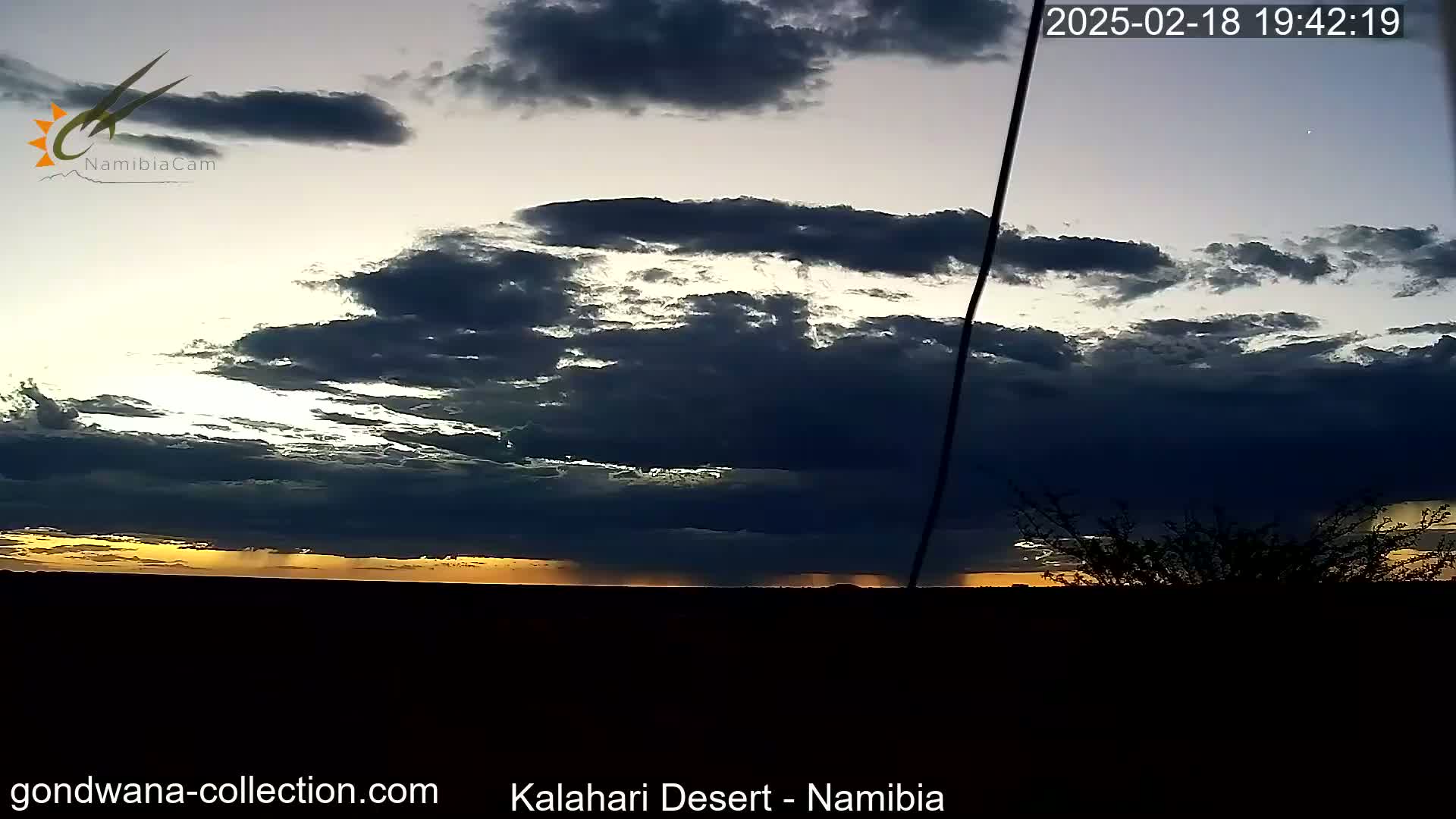 A dark, cloudy sunset casts a golden light on the horizon over a flat, dark landscape.