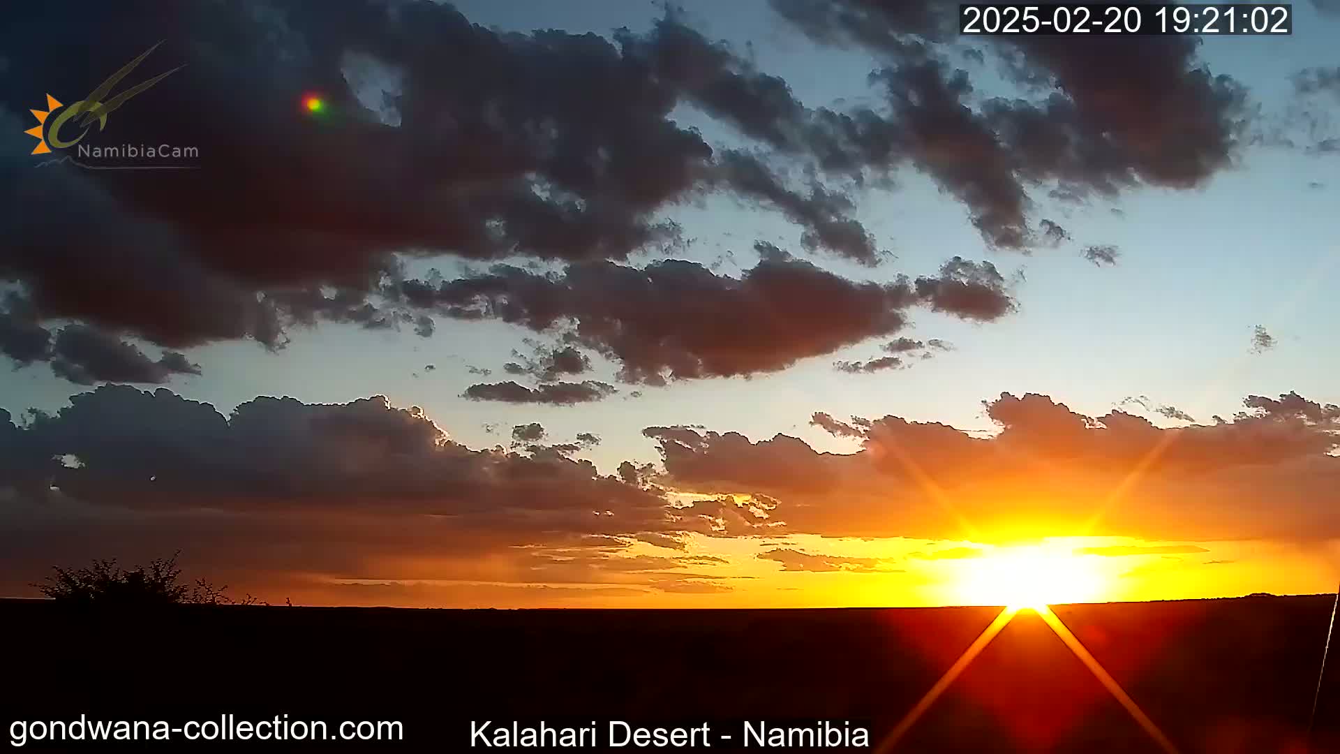 A vibrant sunset casts an orange and yellow glow across a cloudy sky over a dark, flat landscape.