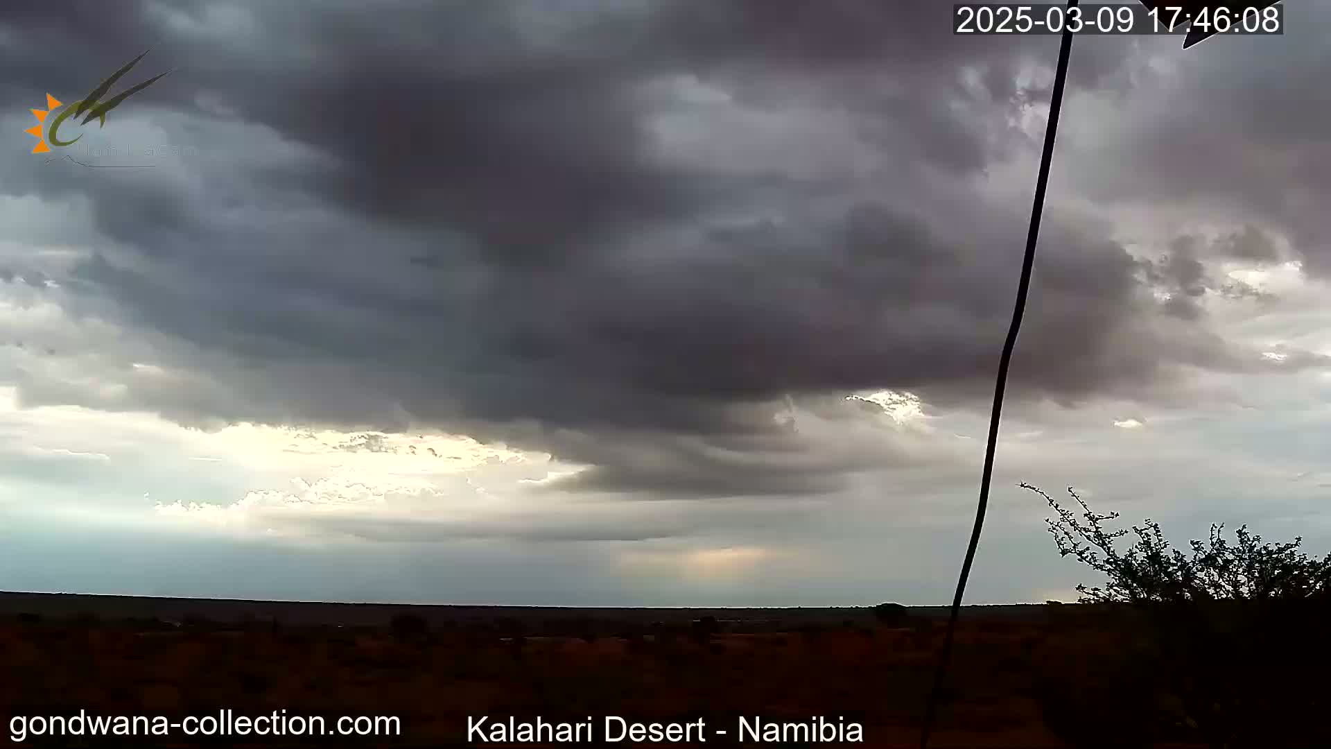 Overcast skies with dark, heavy clouds hang low over a flat, dark landscape, possibly desert, with a sliver of brighter sky visible near the horizon.