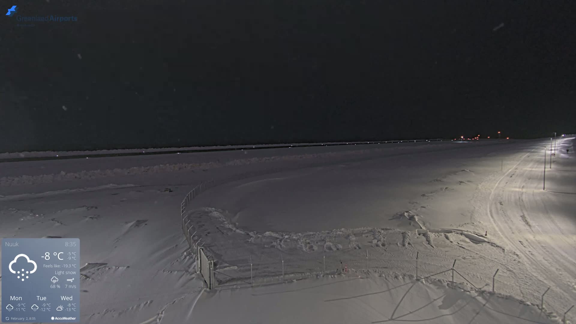 A snow-covered airfield is illuminated at night under light snow.