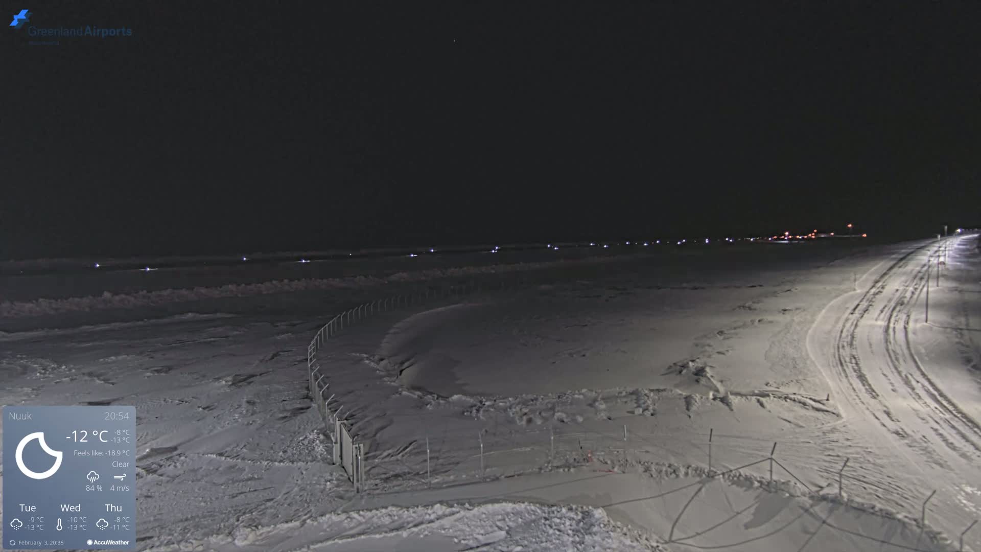 A snow-covered airfield at night with a clear sky and faint lights in the distance.