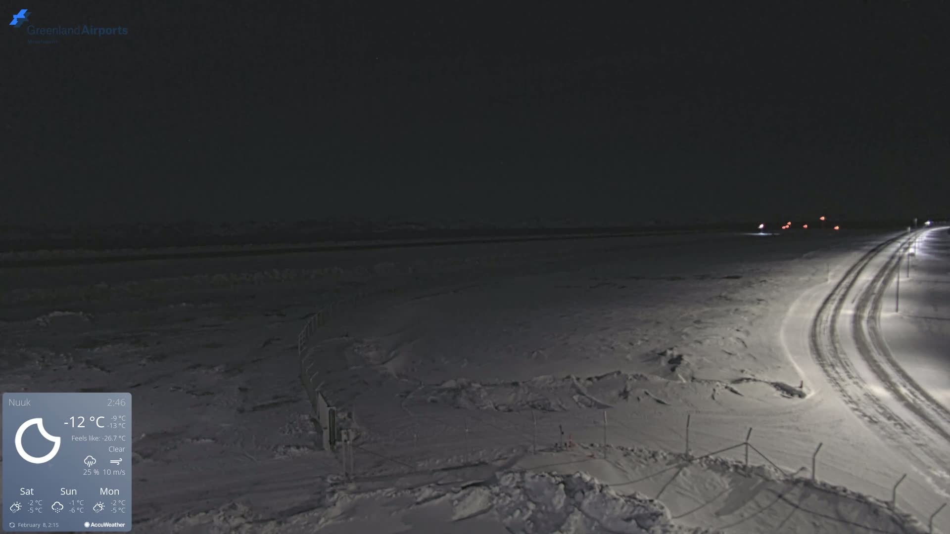 A snow-covered landscape at night, illuminated by streetlights along a road, under clear skies.