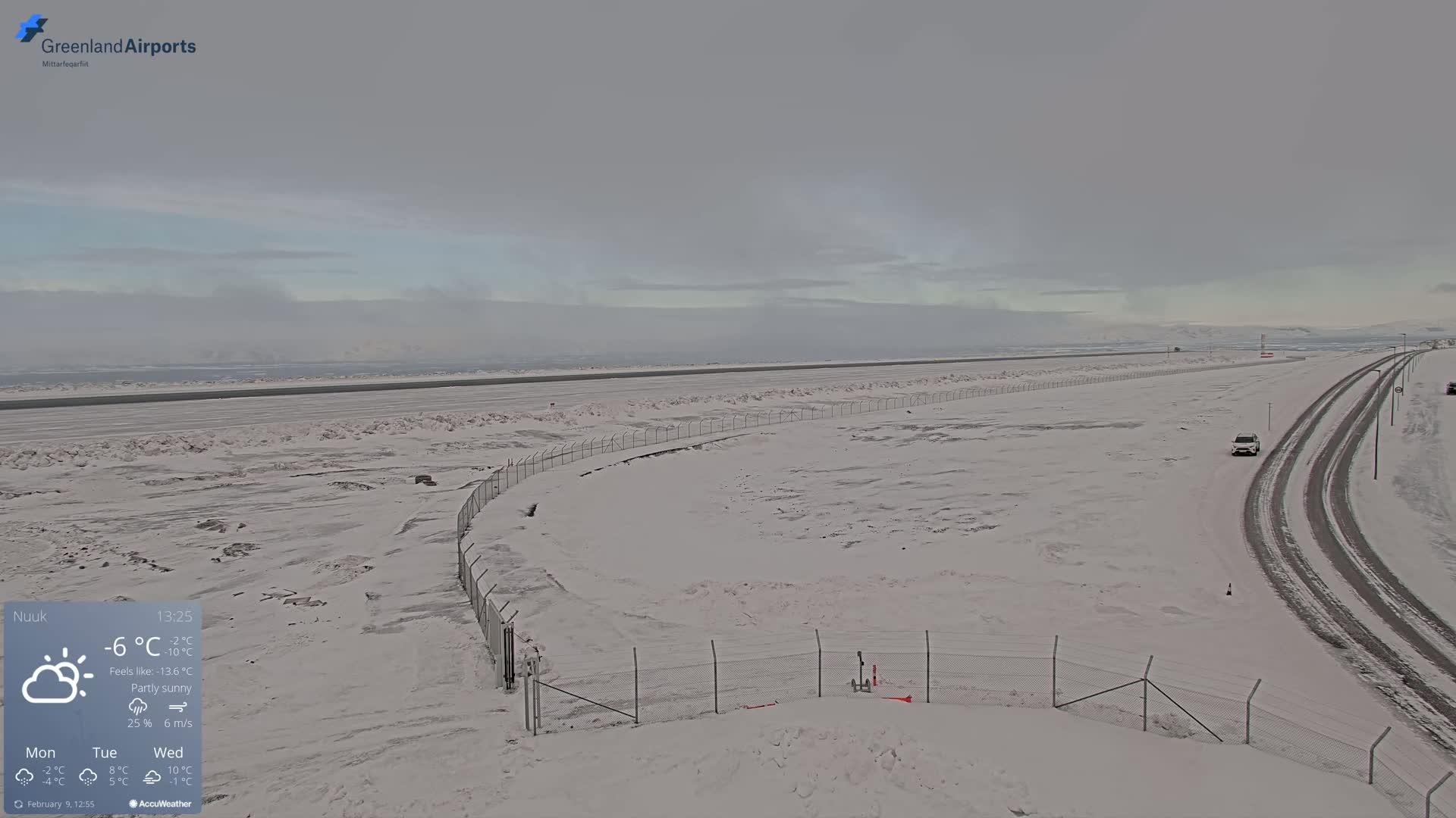A snow-covered airport runway and adjacent road are visible under a partly sunny sky.