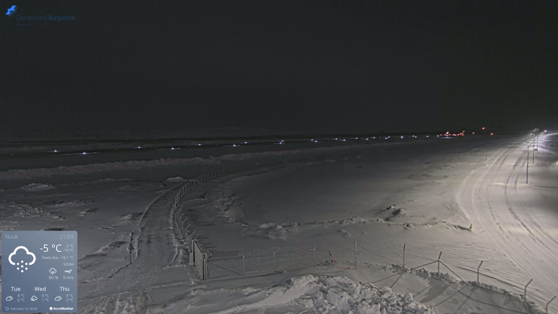 A snow-covered airfield at night under a dark sky with light snow falling.