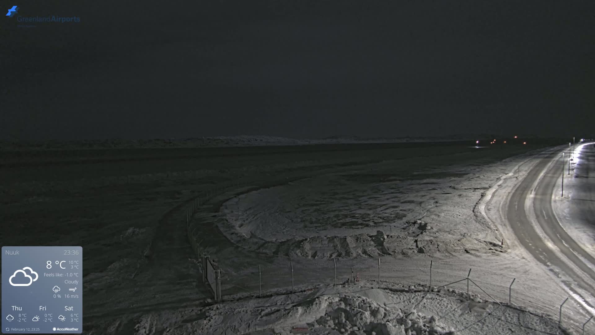 A snow-covered, dark landscape at night is visible, showing a road with lights and a fenced-in area.