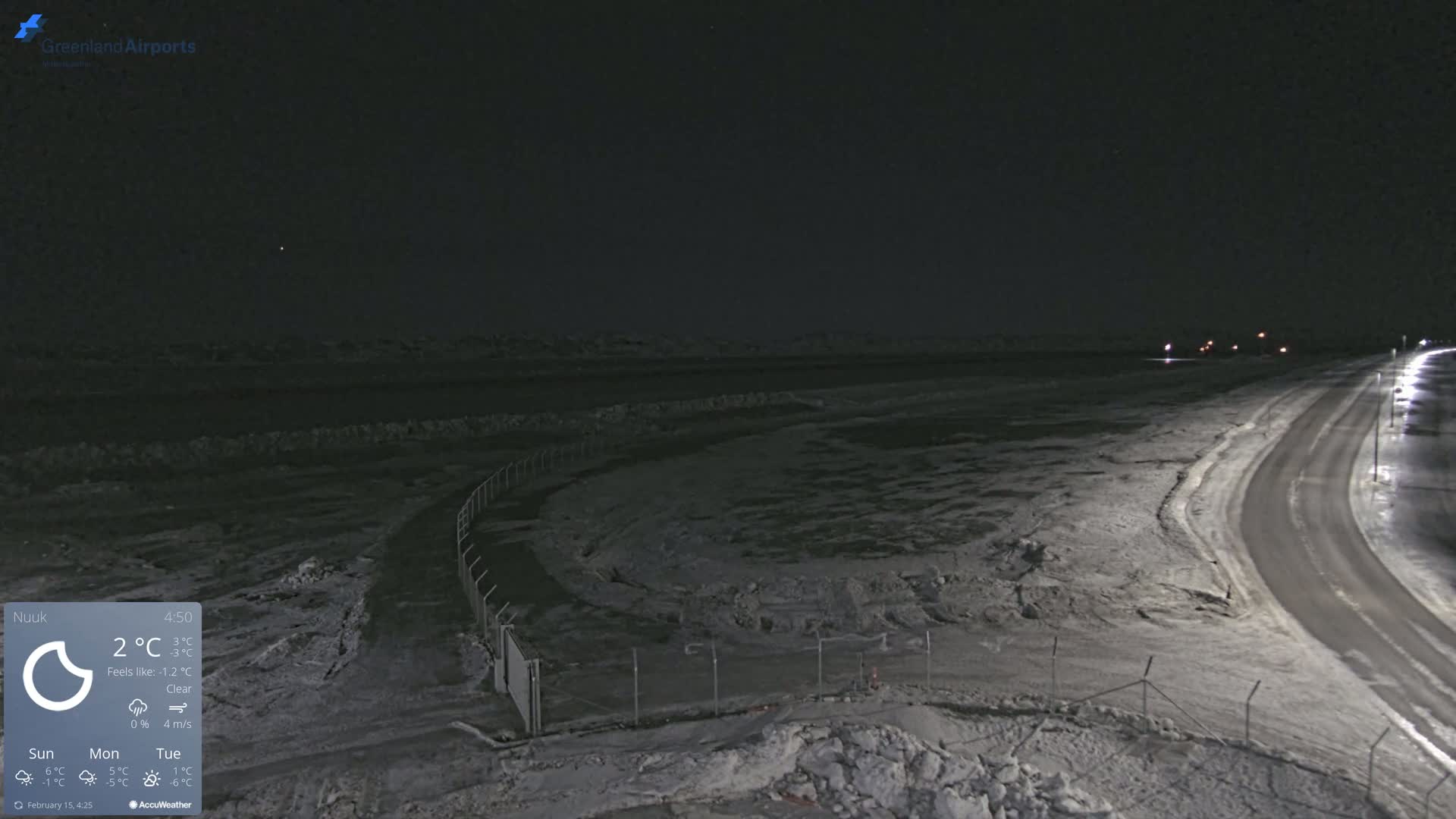 A snow-covered landscape at night is illuminated by streetlights along a curving road, under a clear sky.