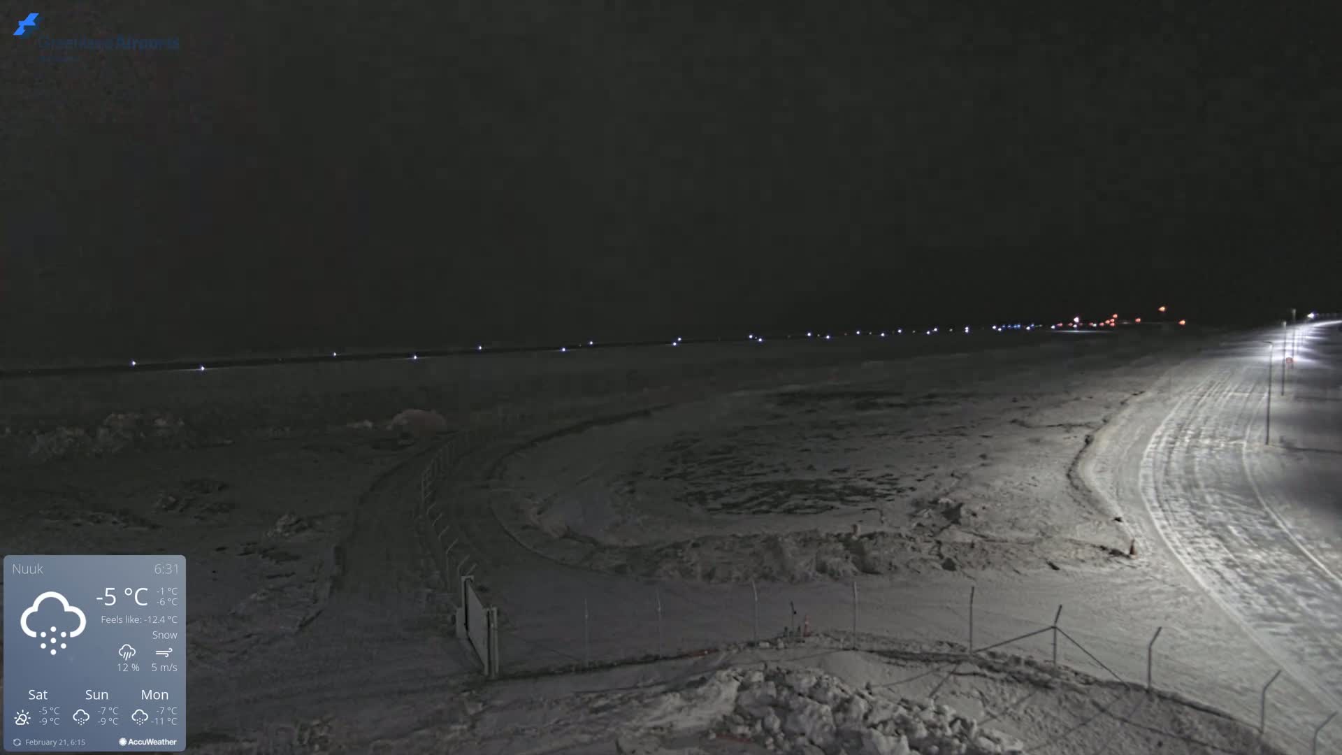 A snow-covered, dimly lit landscape at night, with a road curving into the distance under a dark sky.