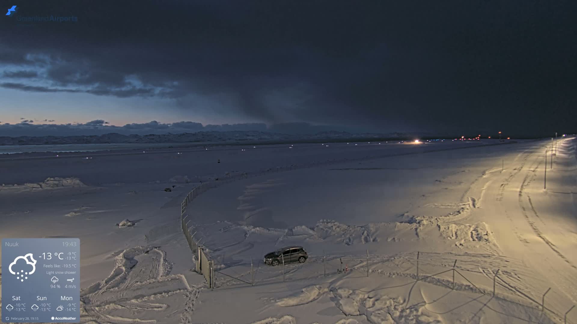 A snow-covered airfield at night under a dark, cloudy sky with a light snow shower.