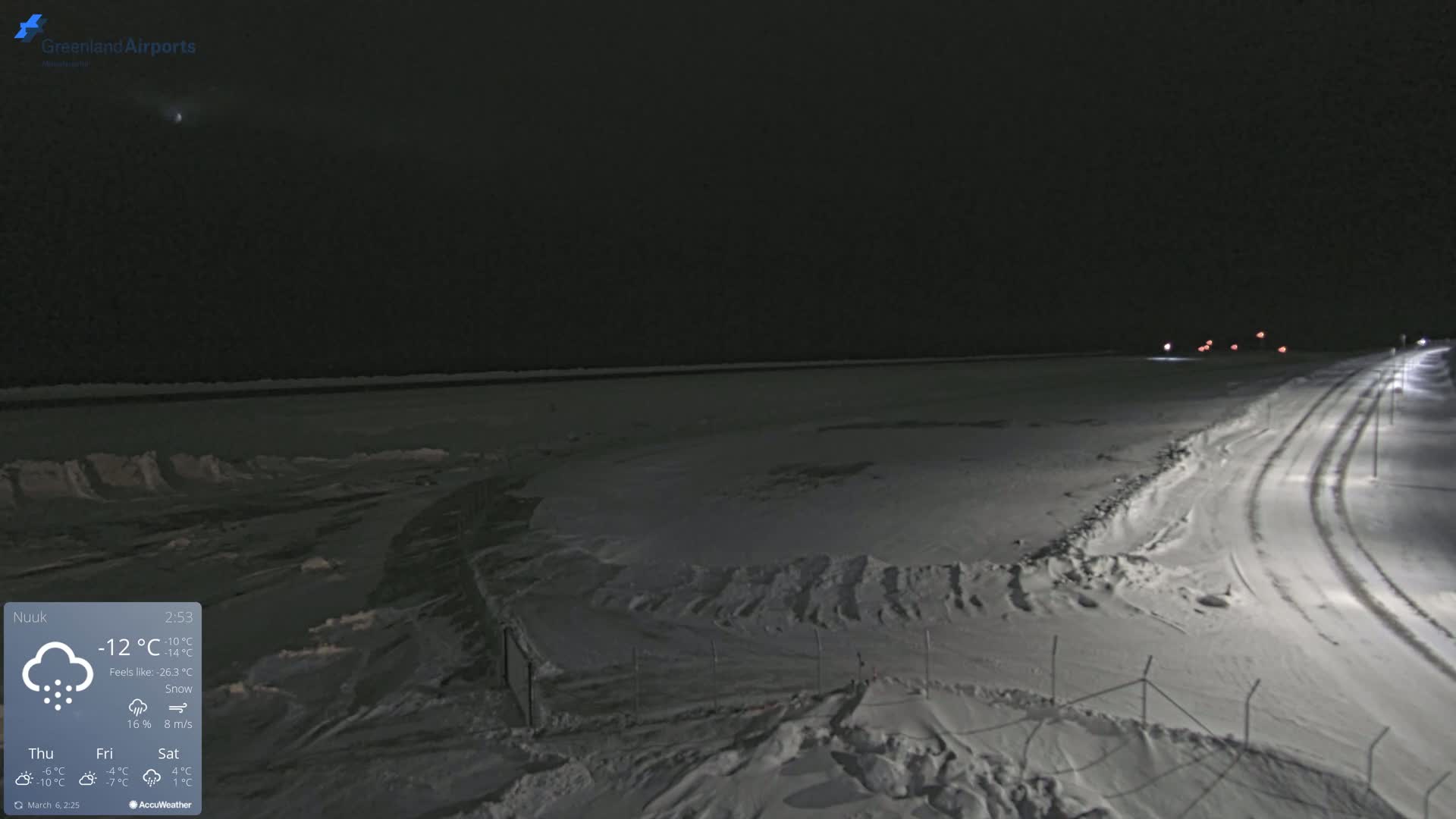 A snow-covered landscape at night, with a road curving into the distance under partly cloudy skies.