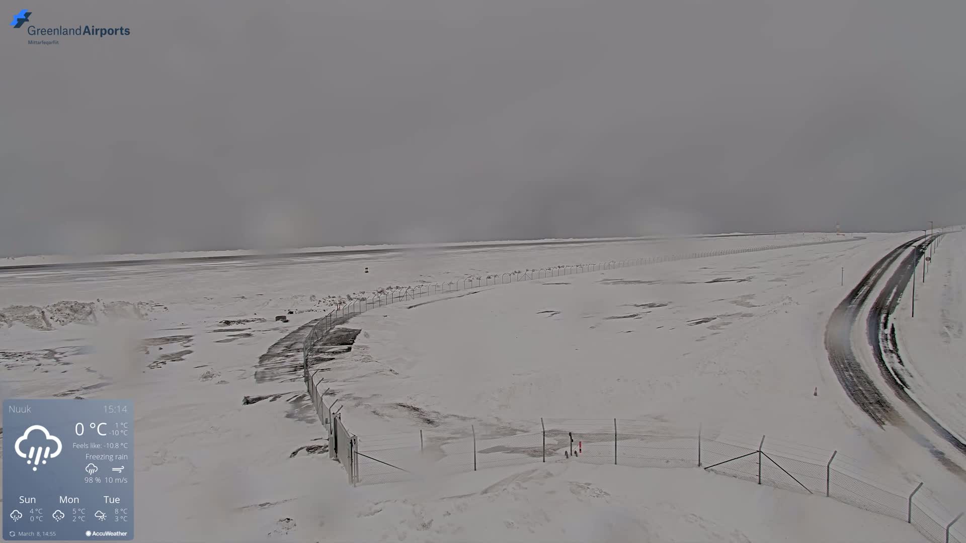 A snow-covered landscape with a road and fence under an overcast sky and freezing rain.