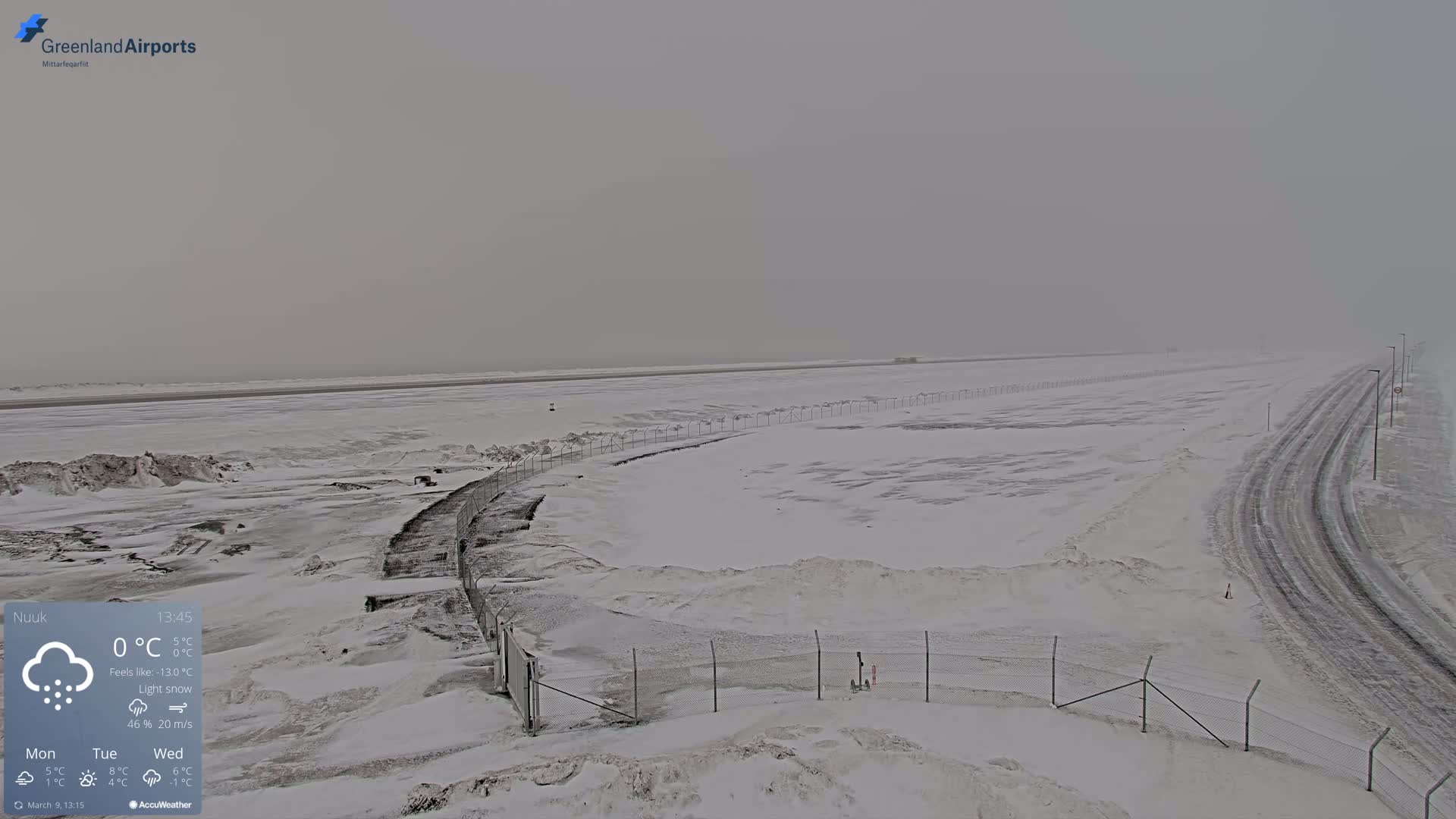 A snow-covered airport runway and road are visible under light snow in overcast conditions.