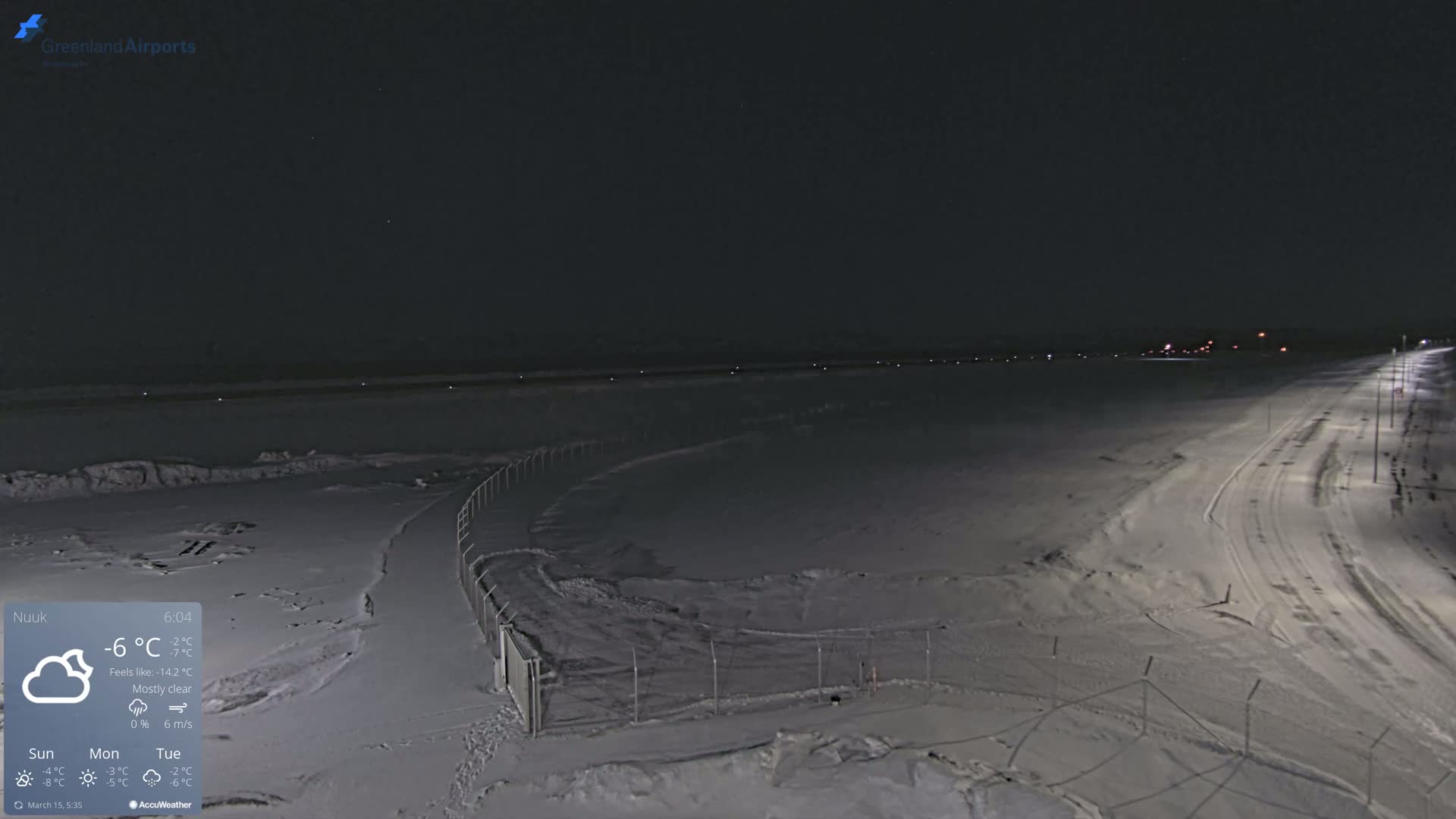 A snow-covered airport tarmac is illuminated at night under a mostly clear sky.