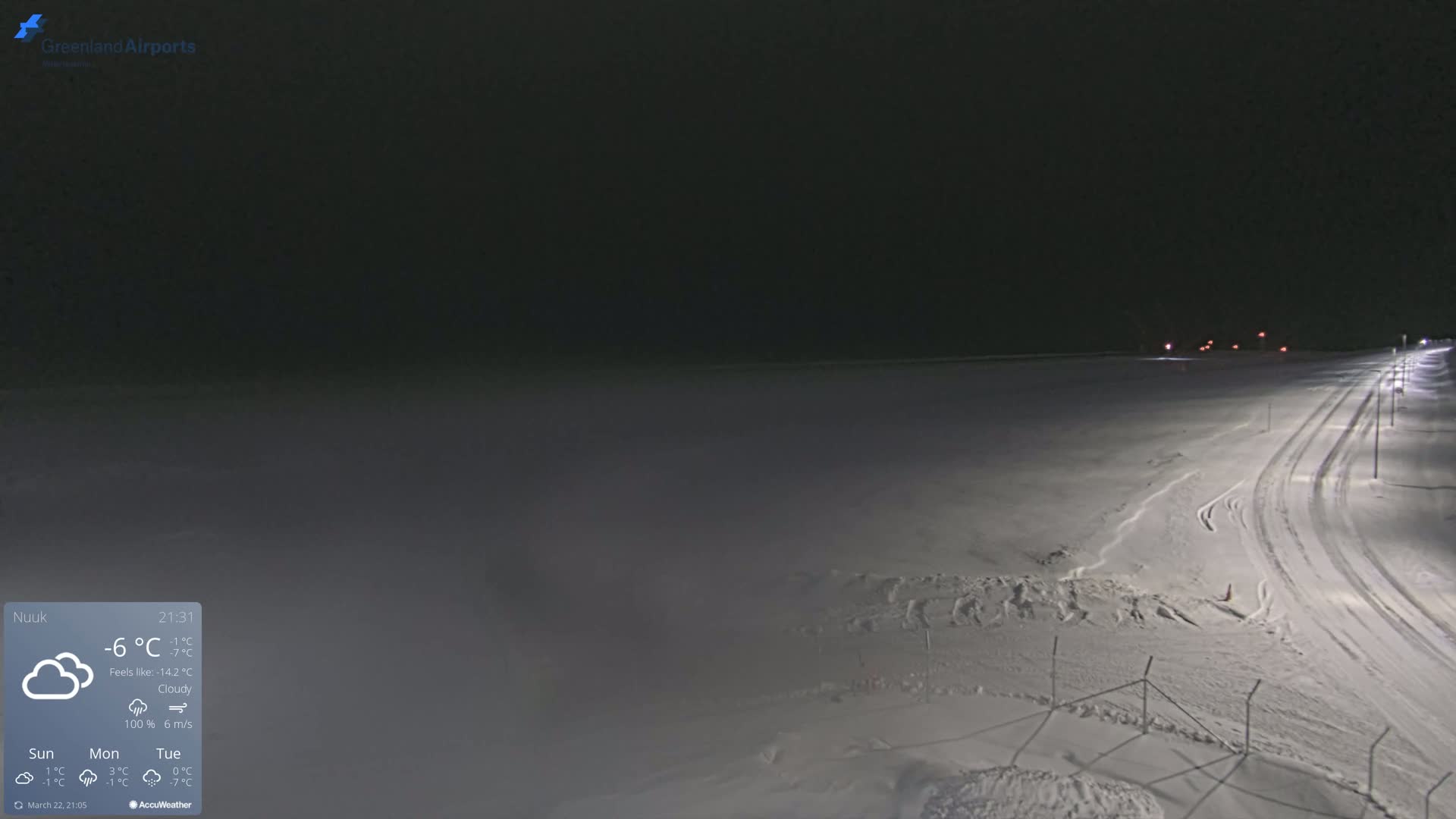 A snow-covered airfield is illuminated at night under cloudy skies.