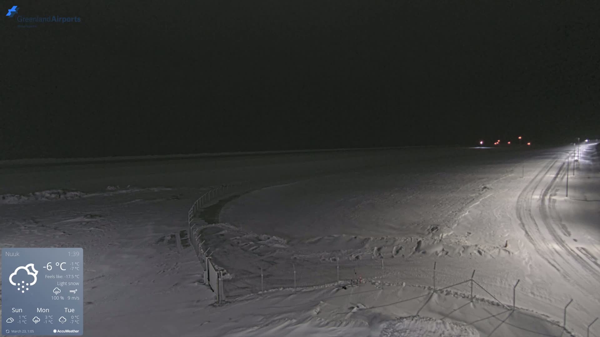 A snow-covered, dimly lit airfield is seen at night under light snow.
