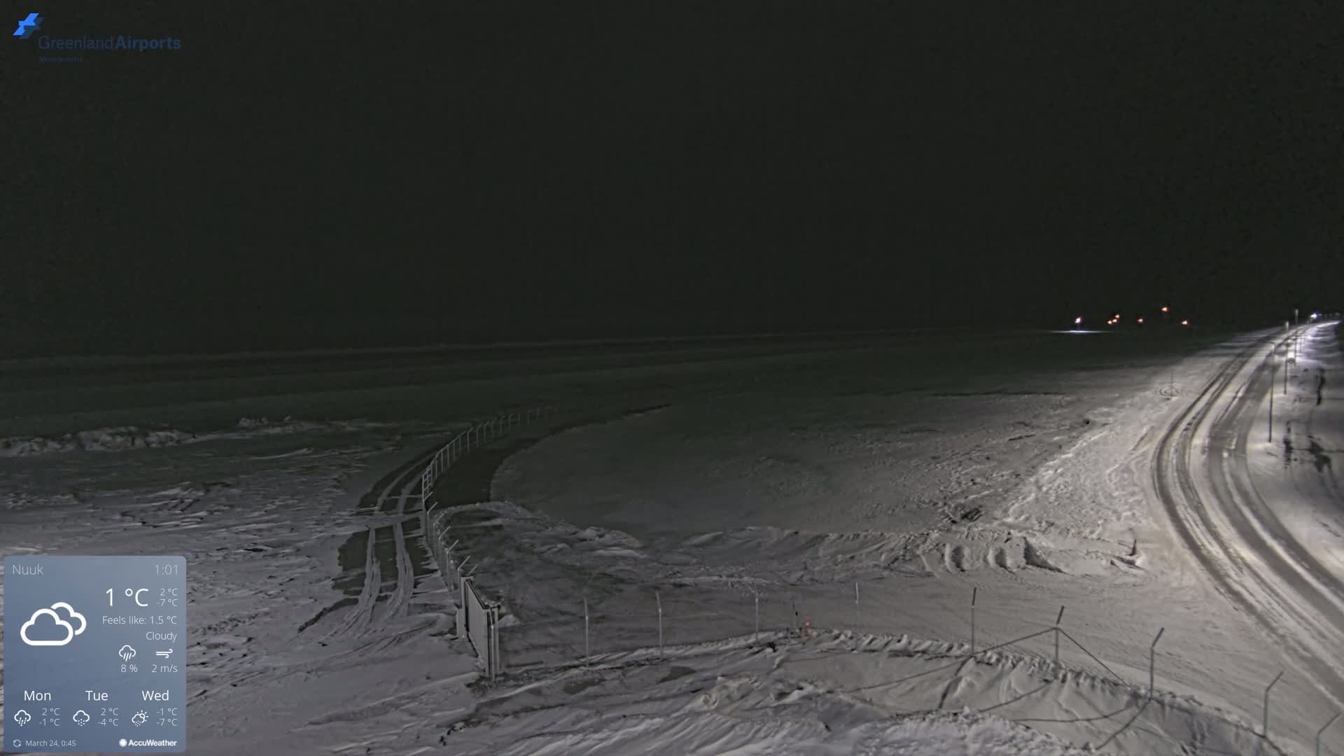 A snow-covered landscape is visible at night under cloudy skies, with a road and fence in the foreground.