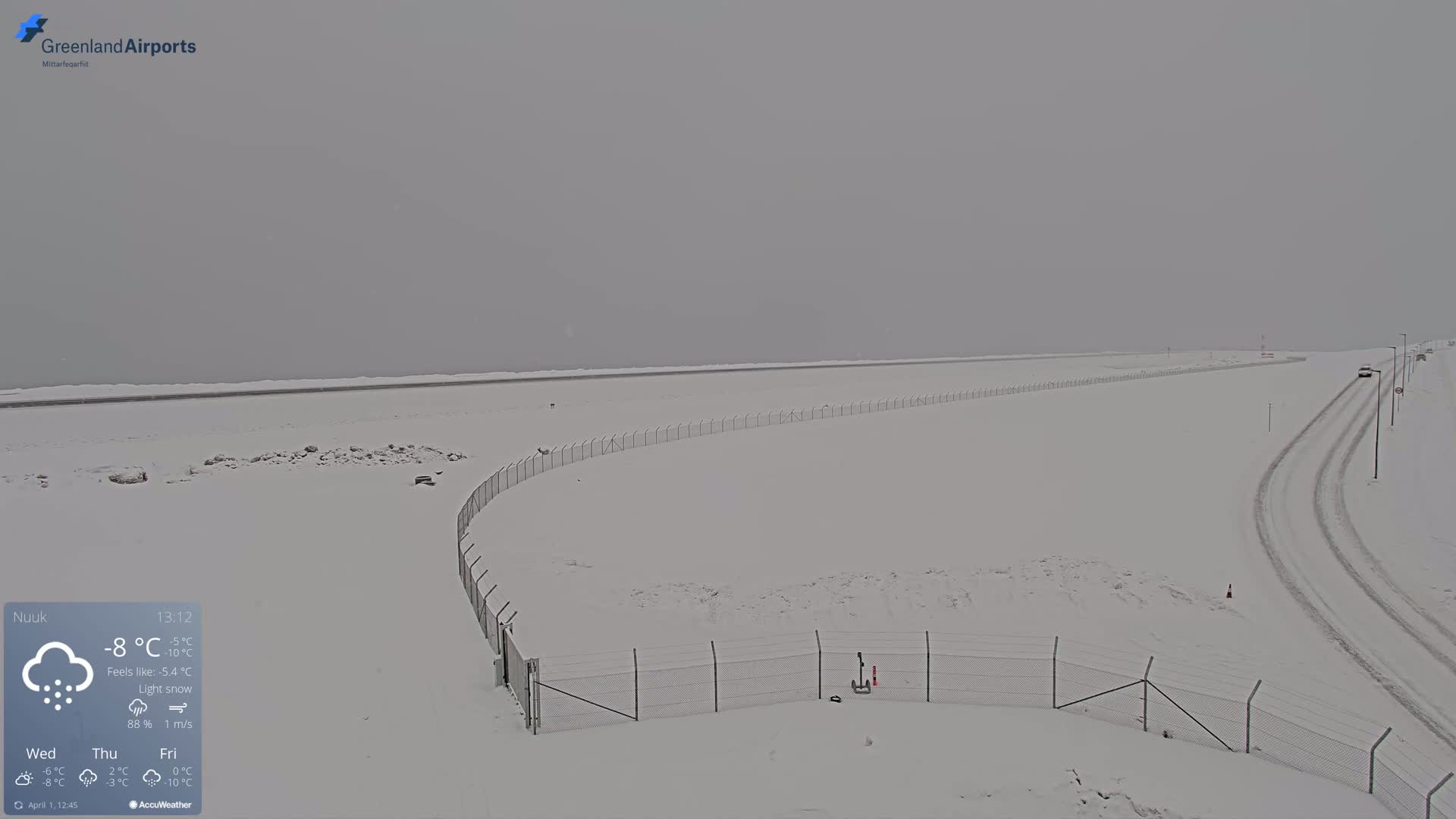 A snow-covered landscape with a chain-link fence and tire tracks in light snow.
