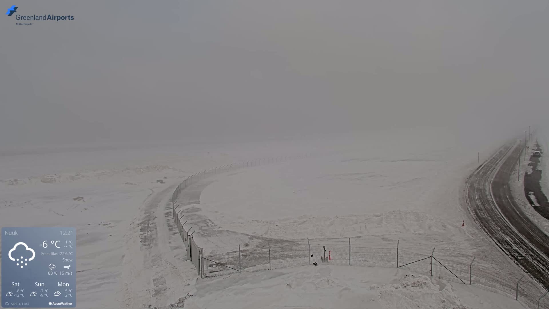 A snow-covered landscape with a road and fence is visible through a heavy snow and fog.
