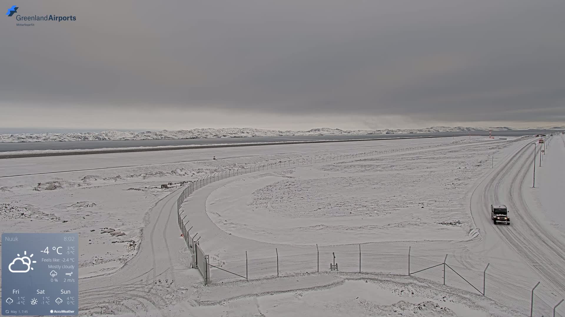A snow-covered airport runway and surrounding area are visible under a mostly cloudy sky.