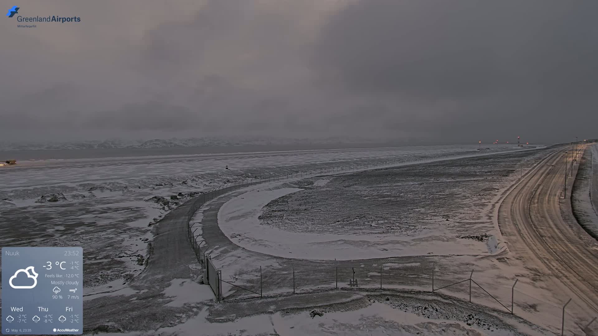 A snow-covered landscape with a road curving through it, under a mostly cloudy, dark sky.