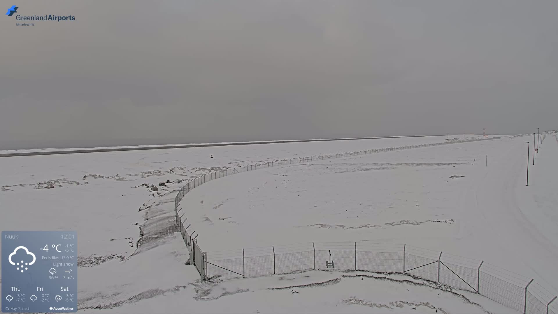 A snow-covered landscape with a chain-link fence curves around a flat expanse, under a light snow.