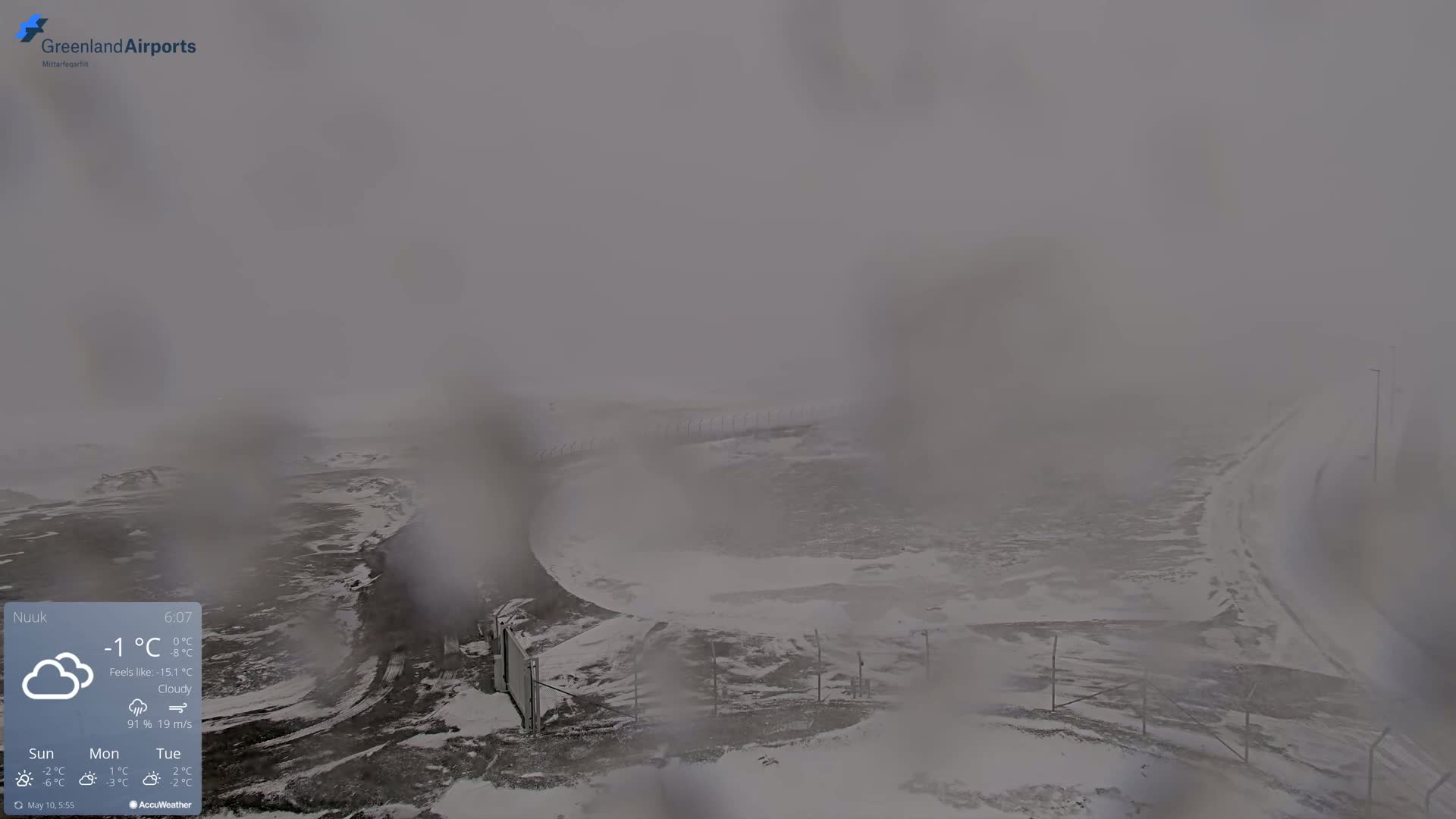 A snow-covered landscape is visible through a hazy, cloudy atmosphere in a windy, cold environment.