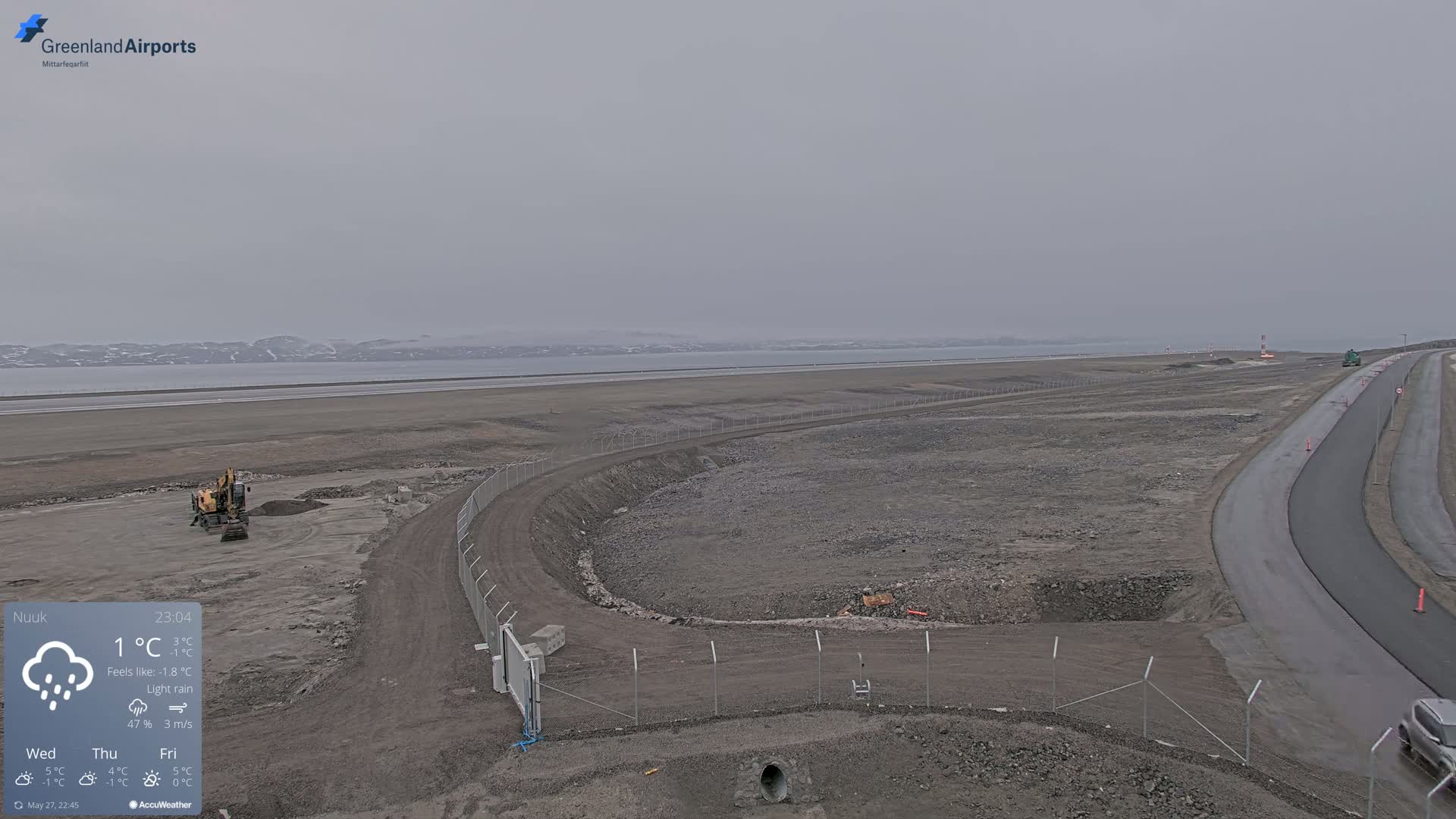 A construction site near a body of water under a light rain and overcast sky.