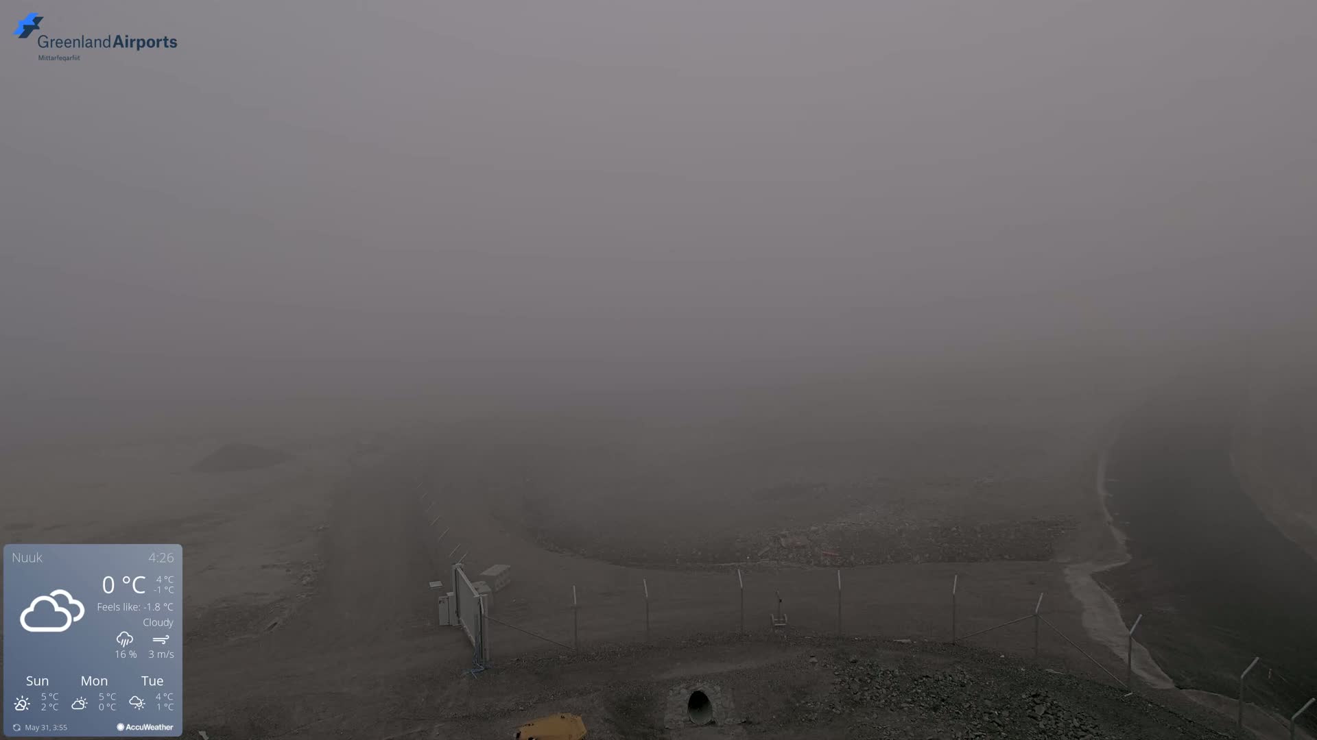 A foggy, outdoor scene shows a fenced-in area with a roadway and a pile of rubble, all obscured by thick fog.