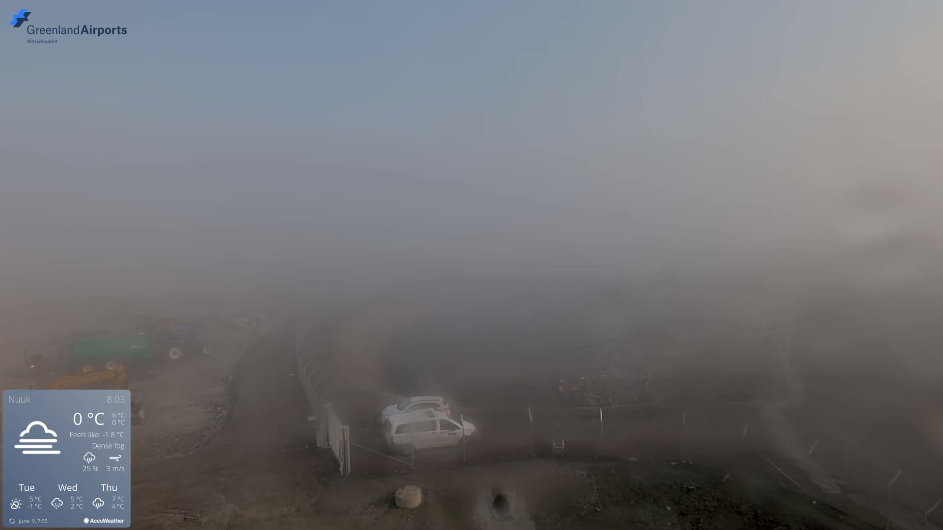 A dense fog obscures the view of a construction site with a few vehicles visible, the scene is outdoors.