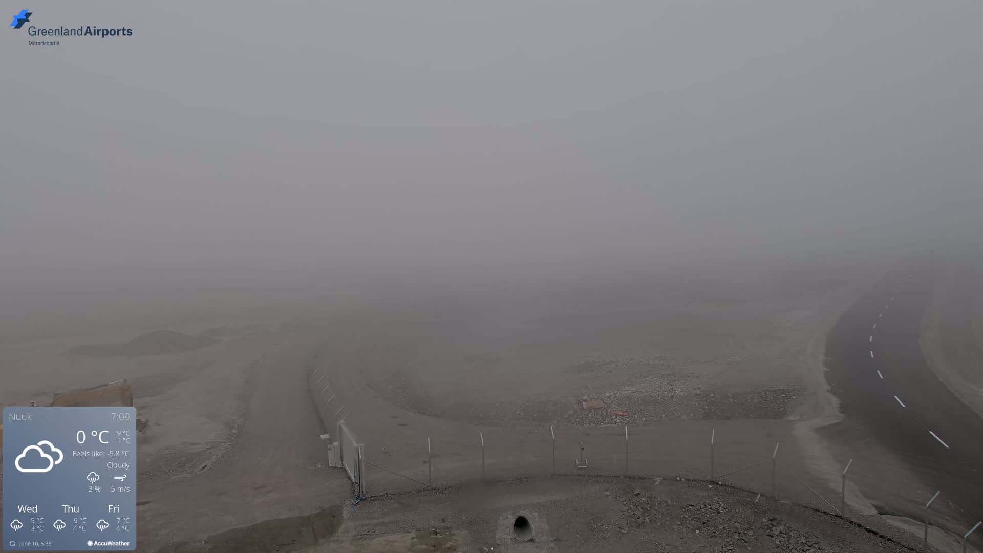 A foggy, overcast scene shows a roadway curving around a section of what appears to be a construction or demolition site.