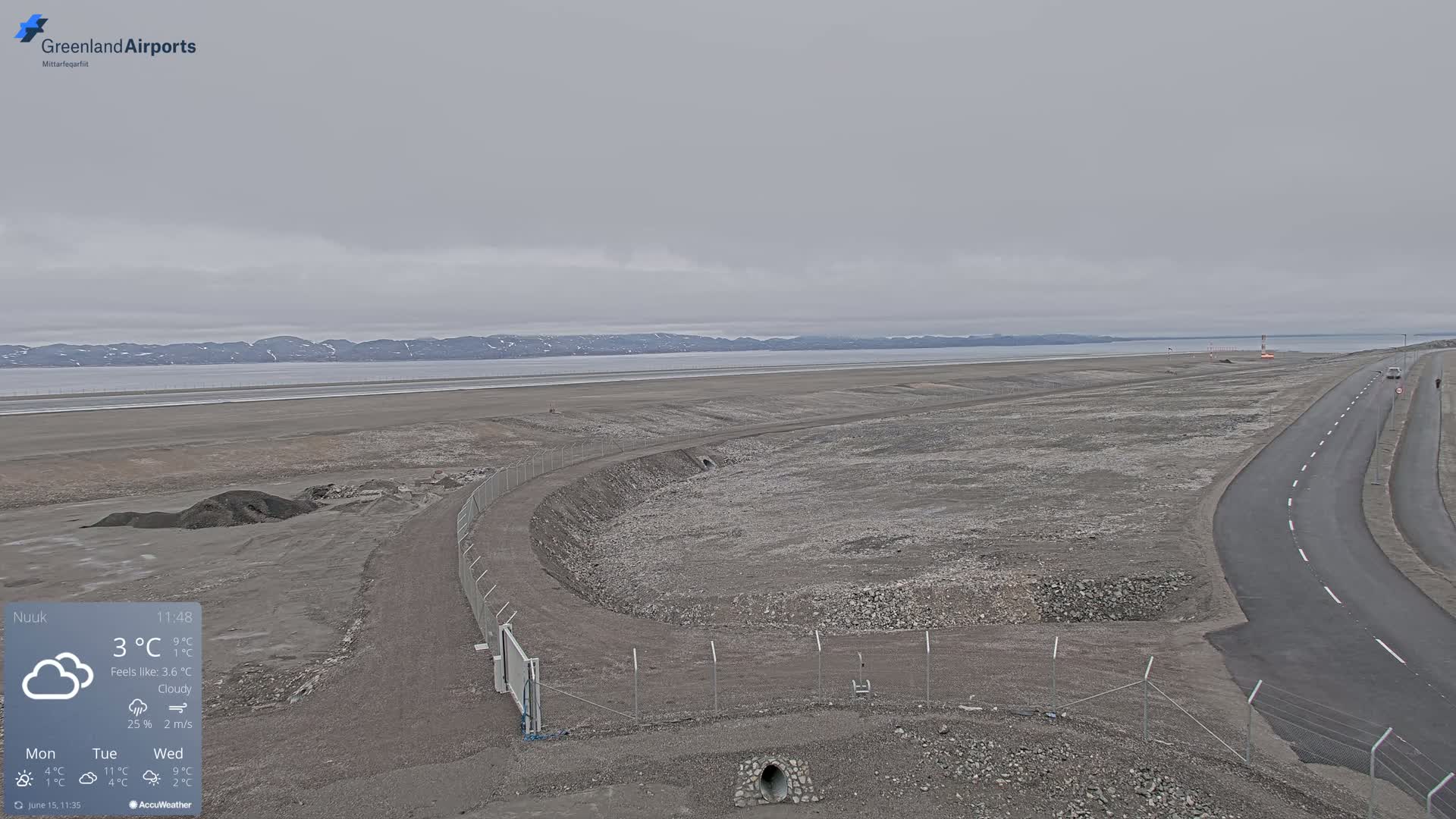 A flat, rocky landscape with a road and a fenced-in area under a cloudy sky.