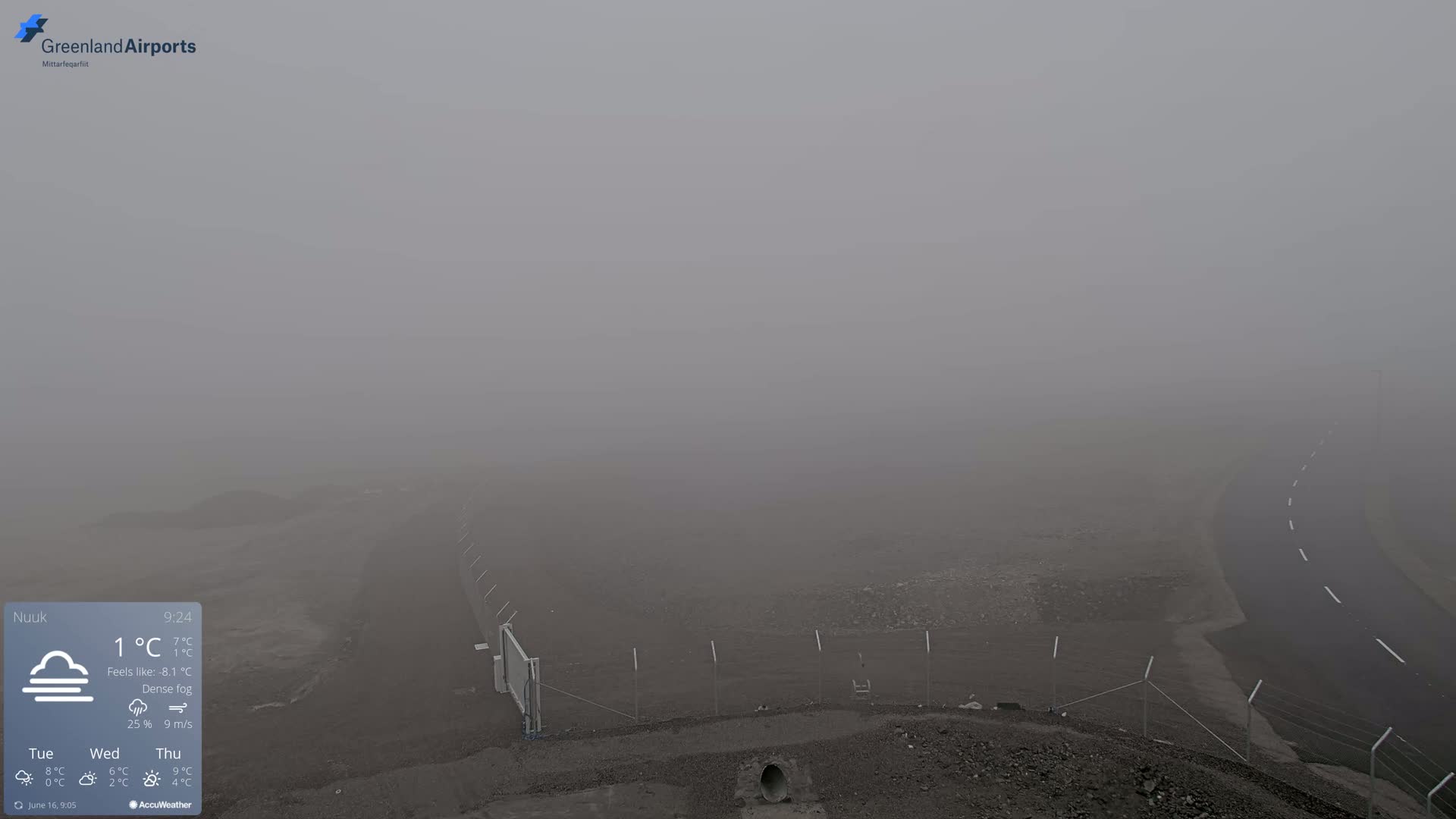 A wide shot of a foggy landscape showing a road and a fence in the dense fog.